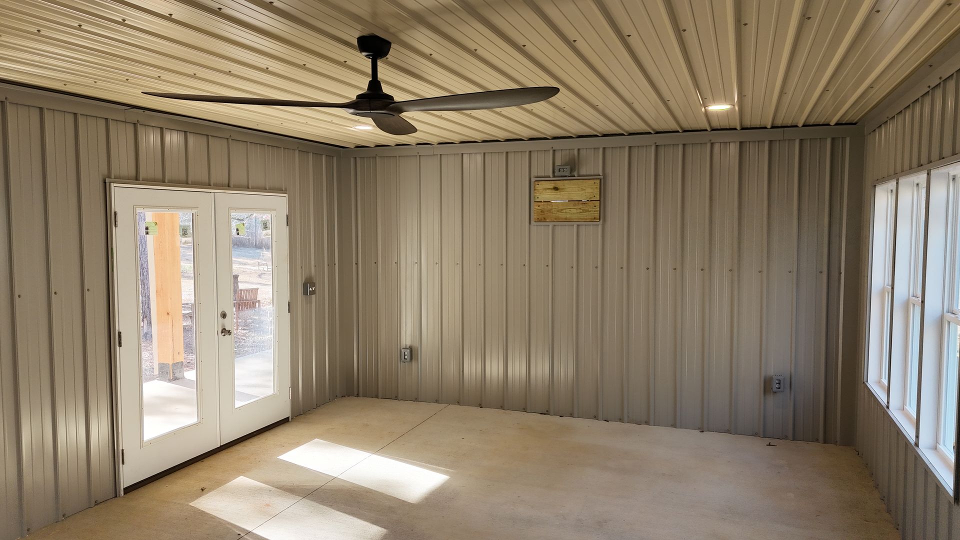Interior view of a room with corrugated metal walls and ceiling, glass French doors, and a ceiling fan.