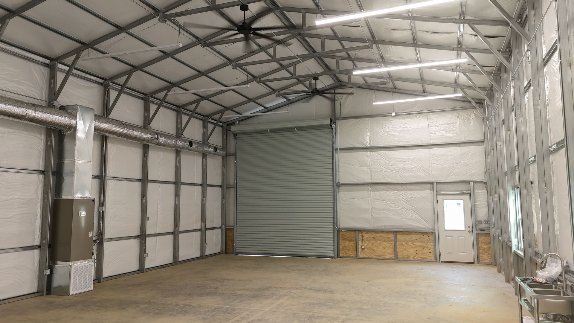 Interior of a metal building with a concrete floor, large door, and insulation.