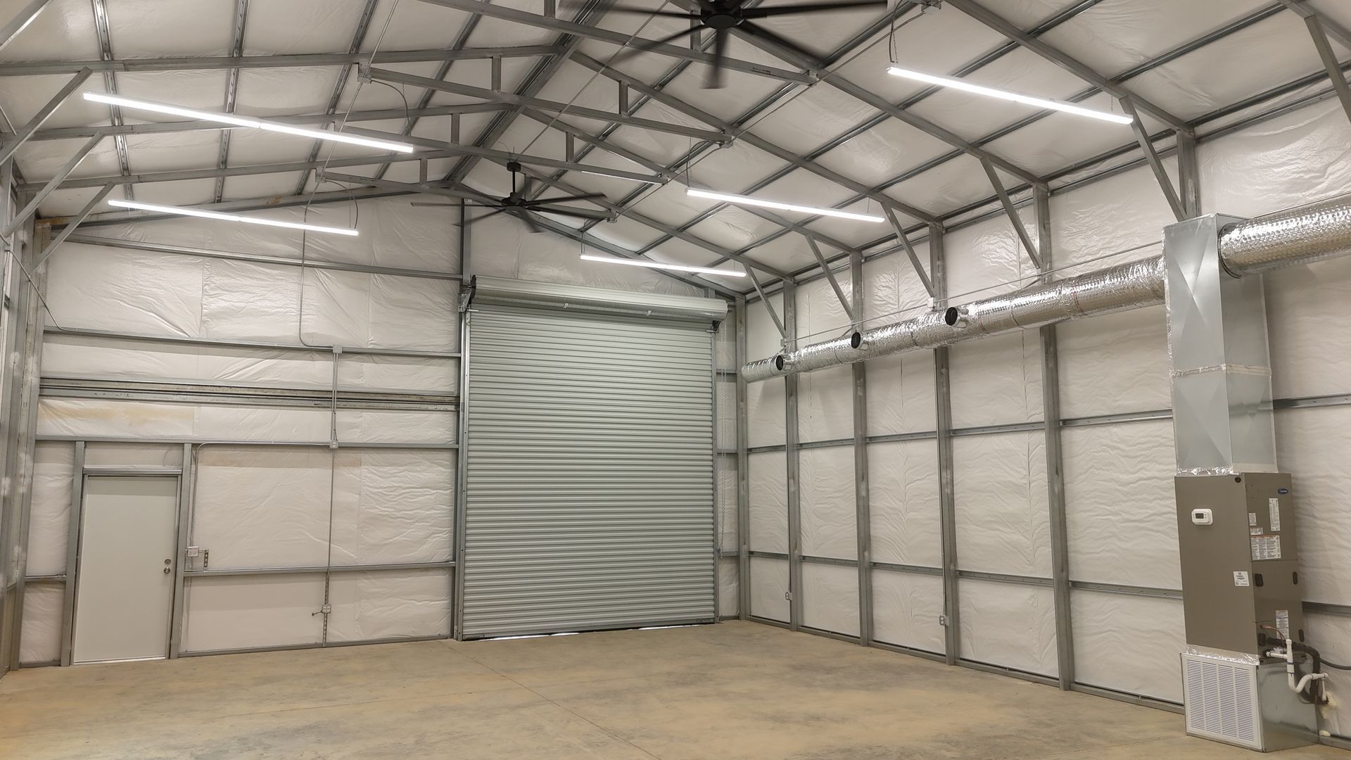 Interior of a metal building with spray foam insulation, overhead lights, and a closed roll-up door.