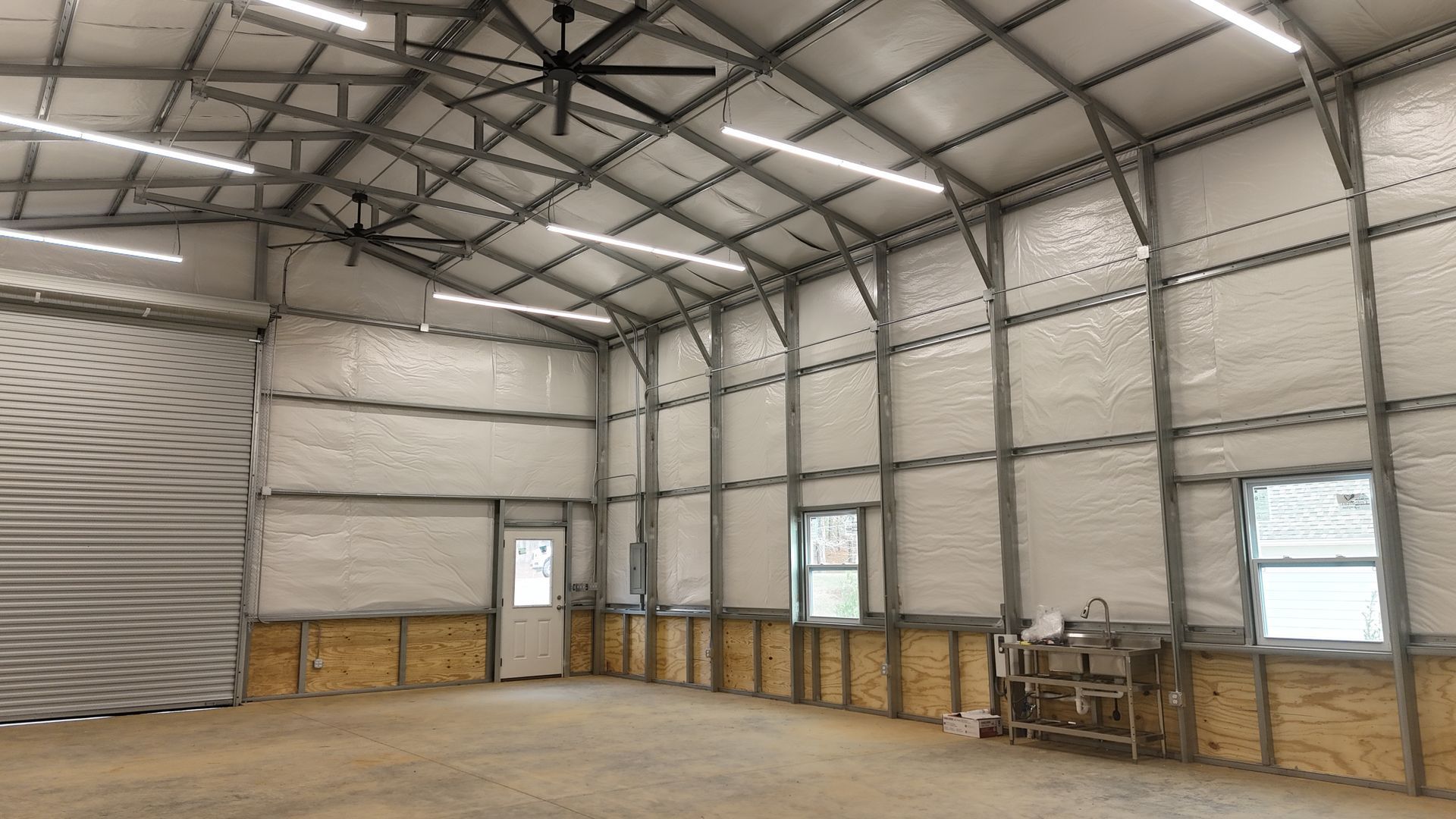 Interior of a large metal building with exposed beams, insulation, and bright LED lights.