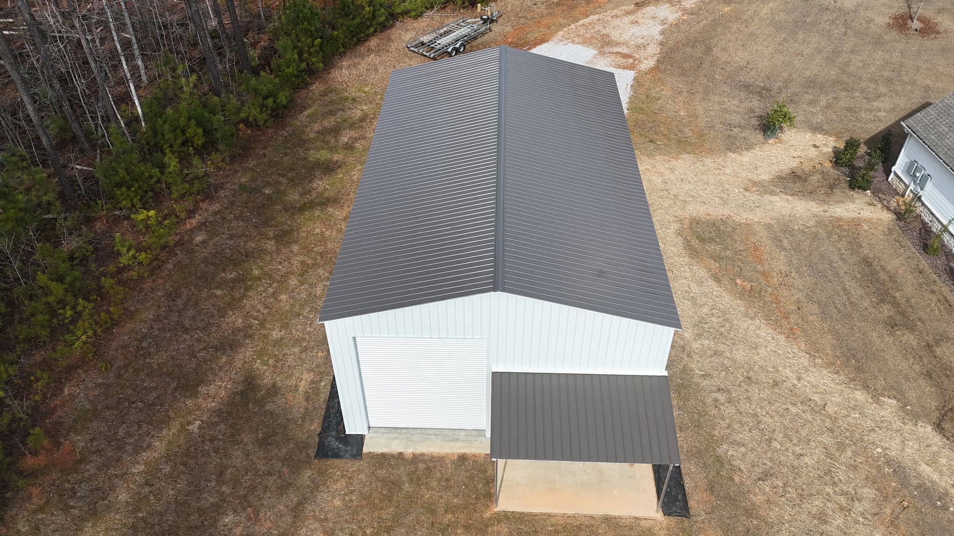 Aerial view of a metal building with a dark gray roof. The walls are light blue-gray, with a small dark roofed extension.