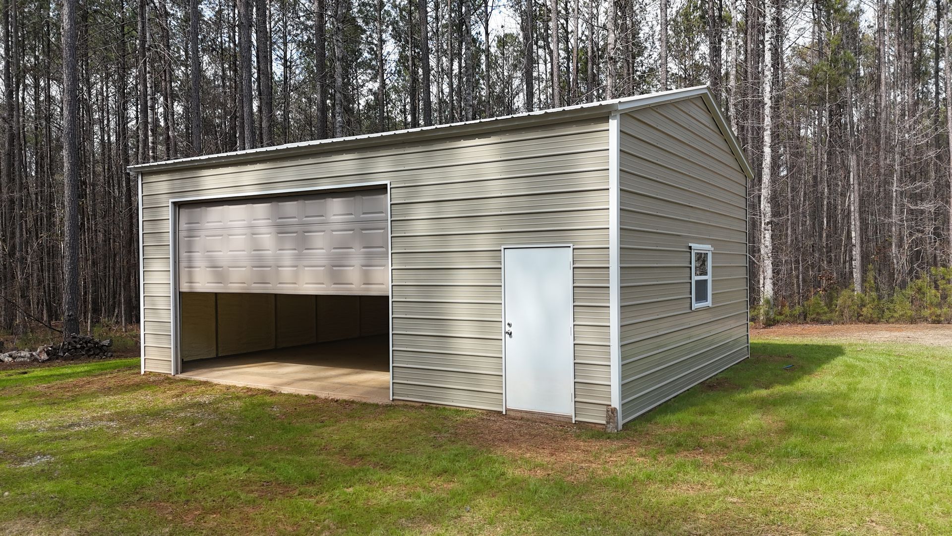 Tan metal garage with roll-up door open, white door, small window, set in grassy area with trees.