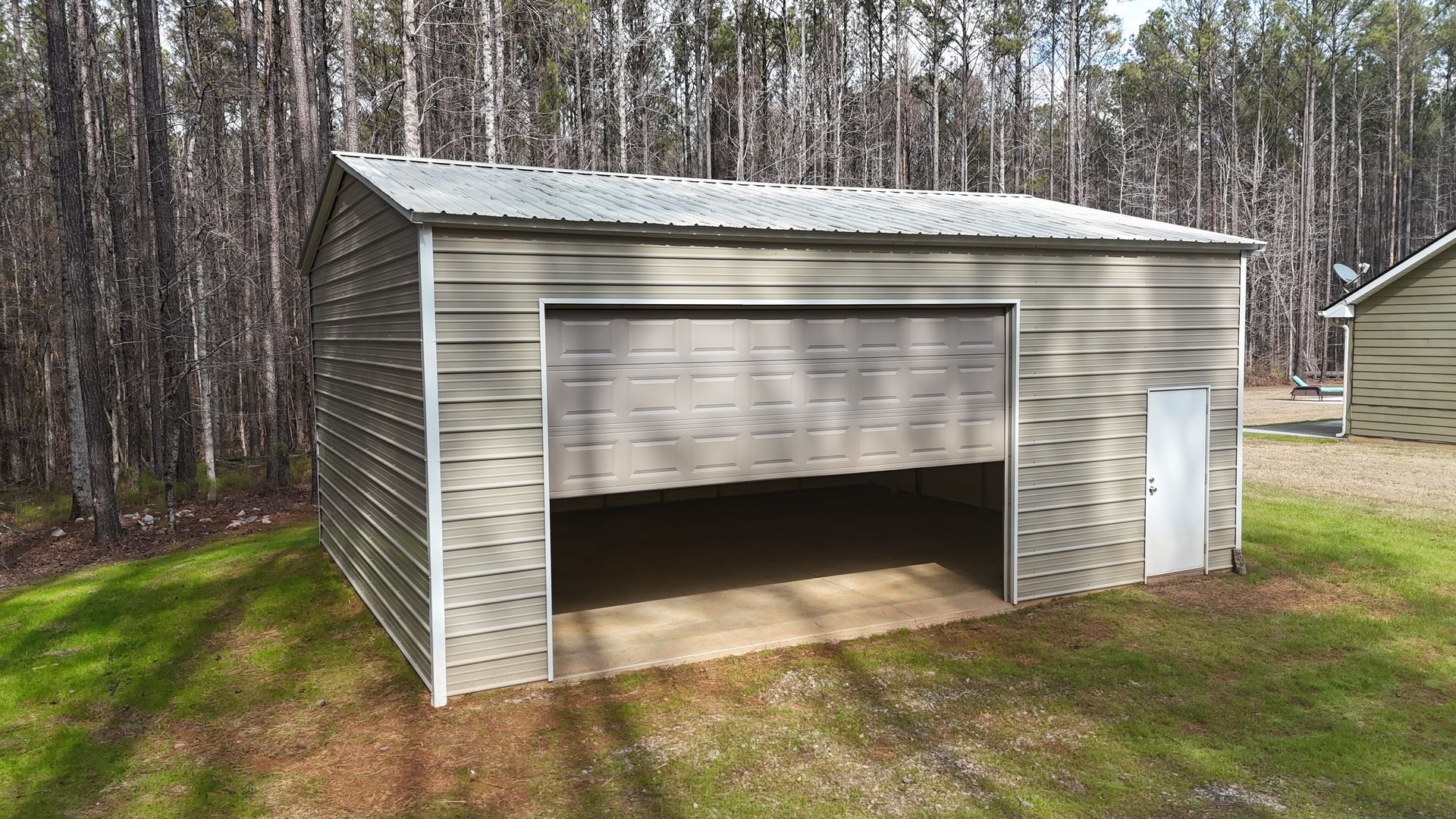 Metal shed with open garage door on a grassy lawn; trees in the background.
