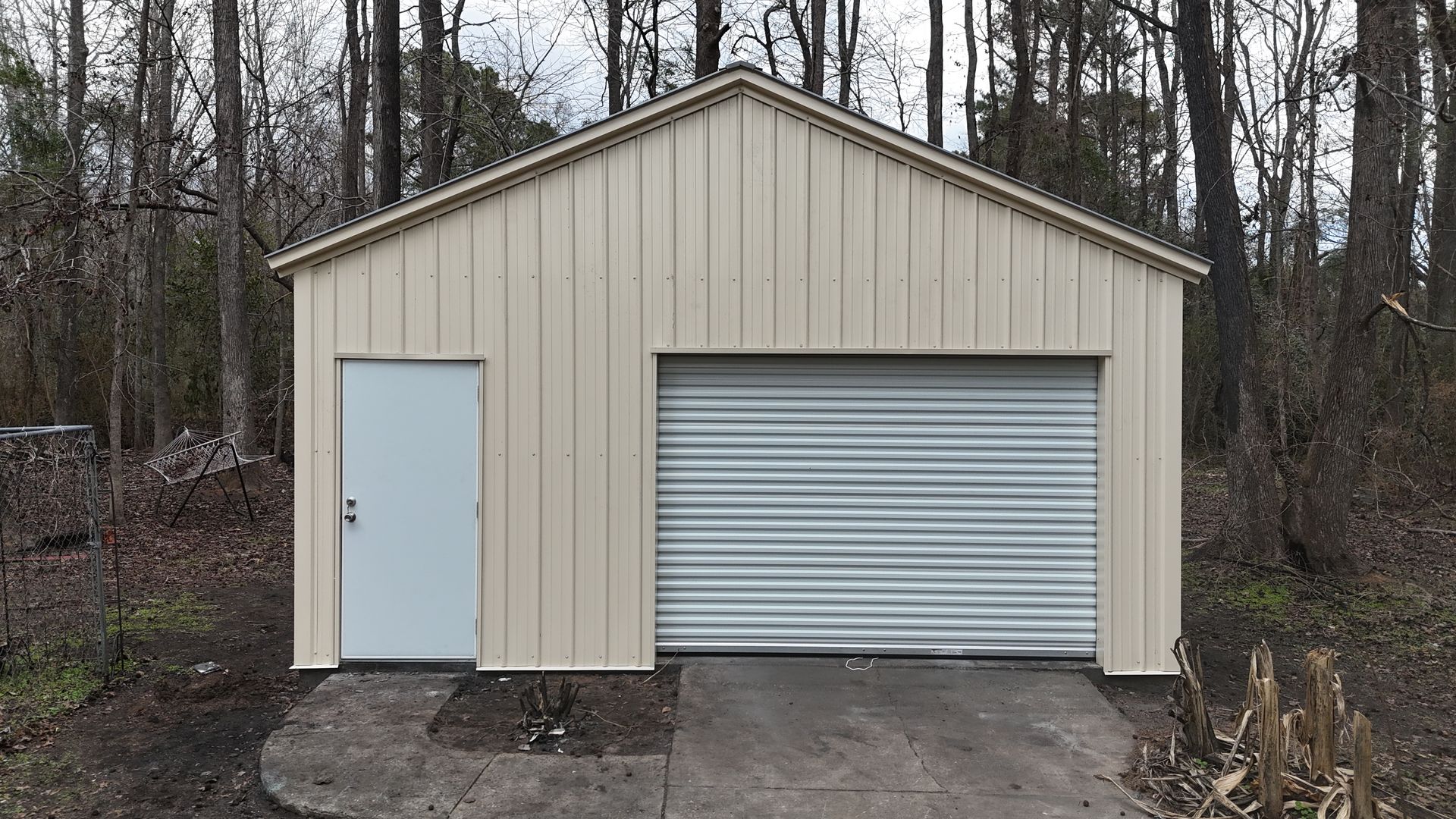 Tan metal shed with a roll-up garage door and a side door, set on a concrete pad.