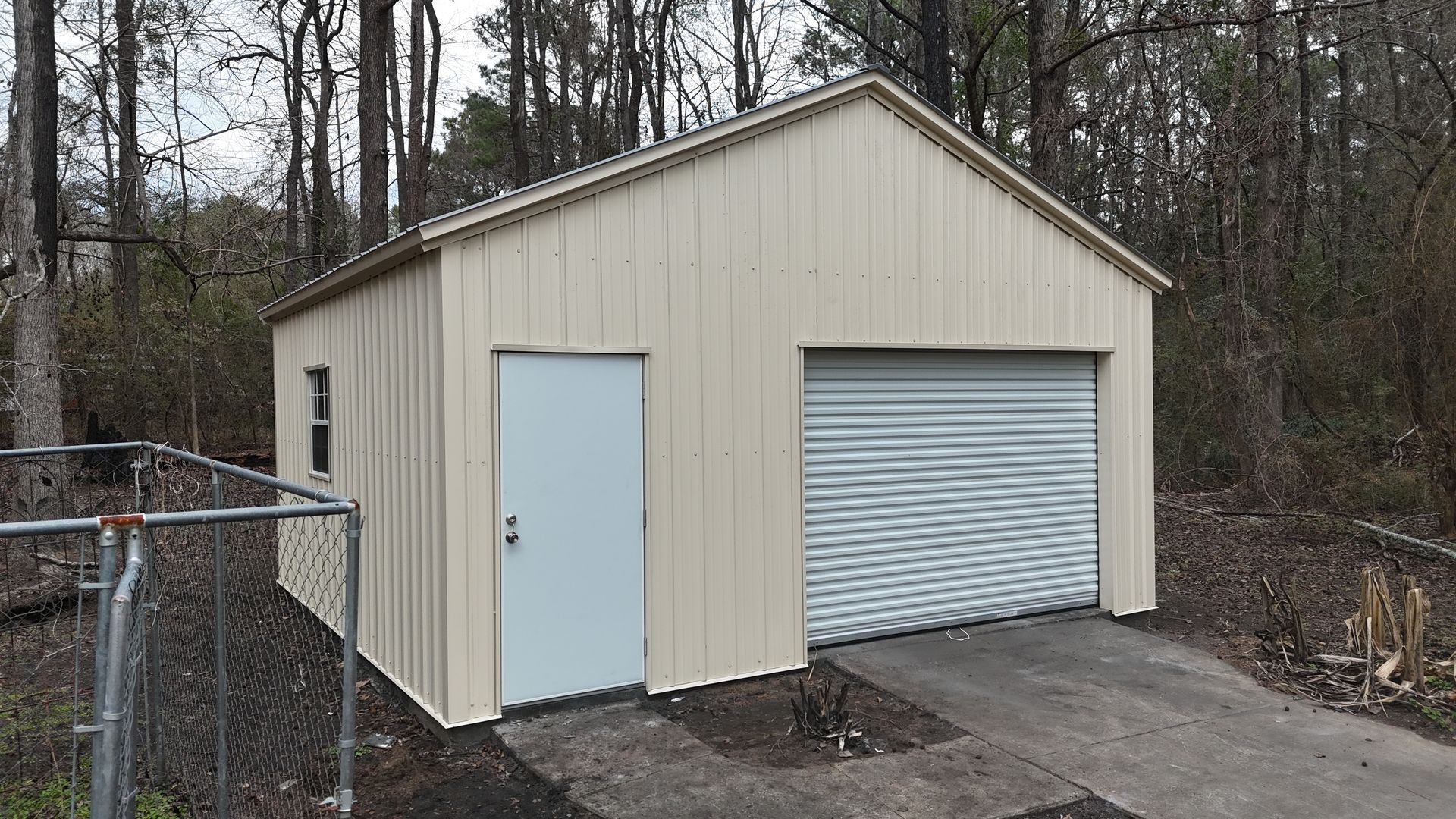 Tan metal garage with a white door, roll-up garage door, and small window on a concrete pad.