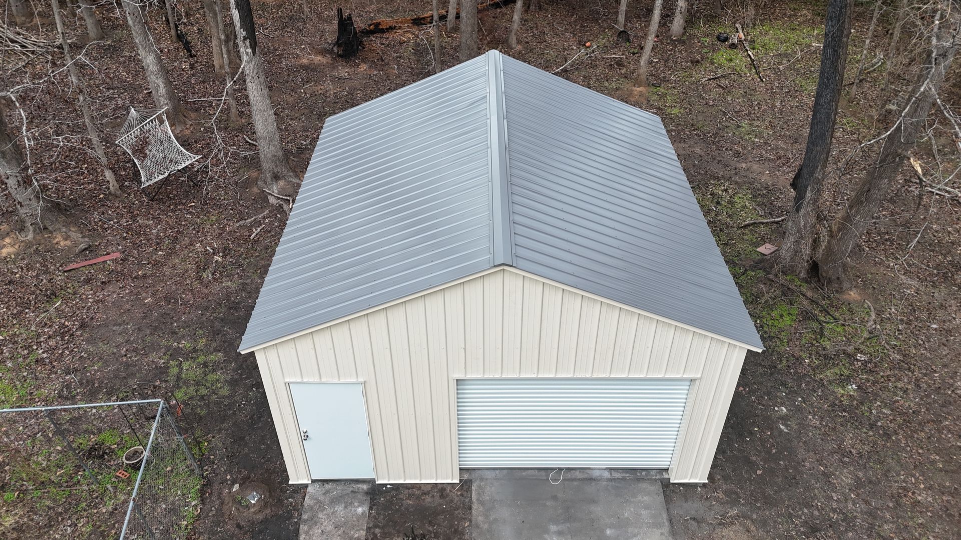 Beige garage with a gray roof in a wooded area.