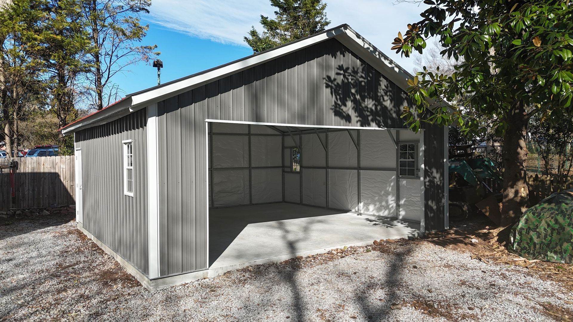 Gray metal garage with open door, gravel driveway, and a blue sky.