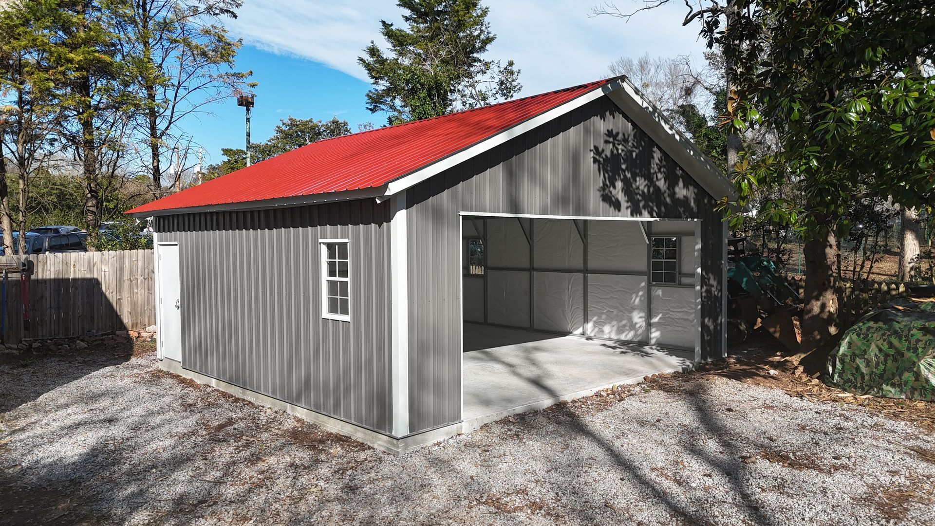 Gray metal garage with red roof and open door, set on gravel.