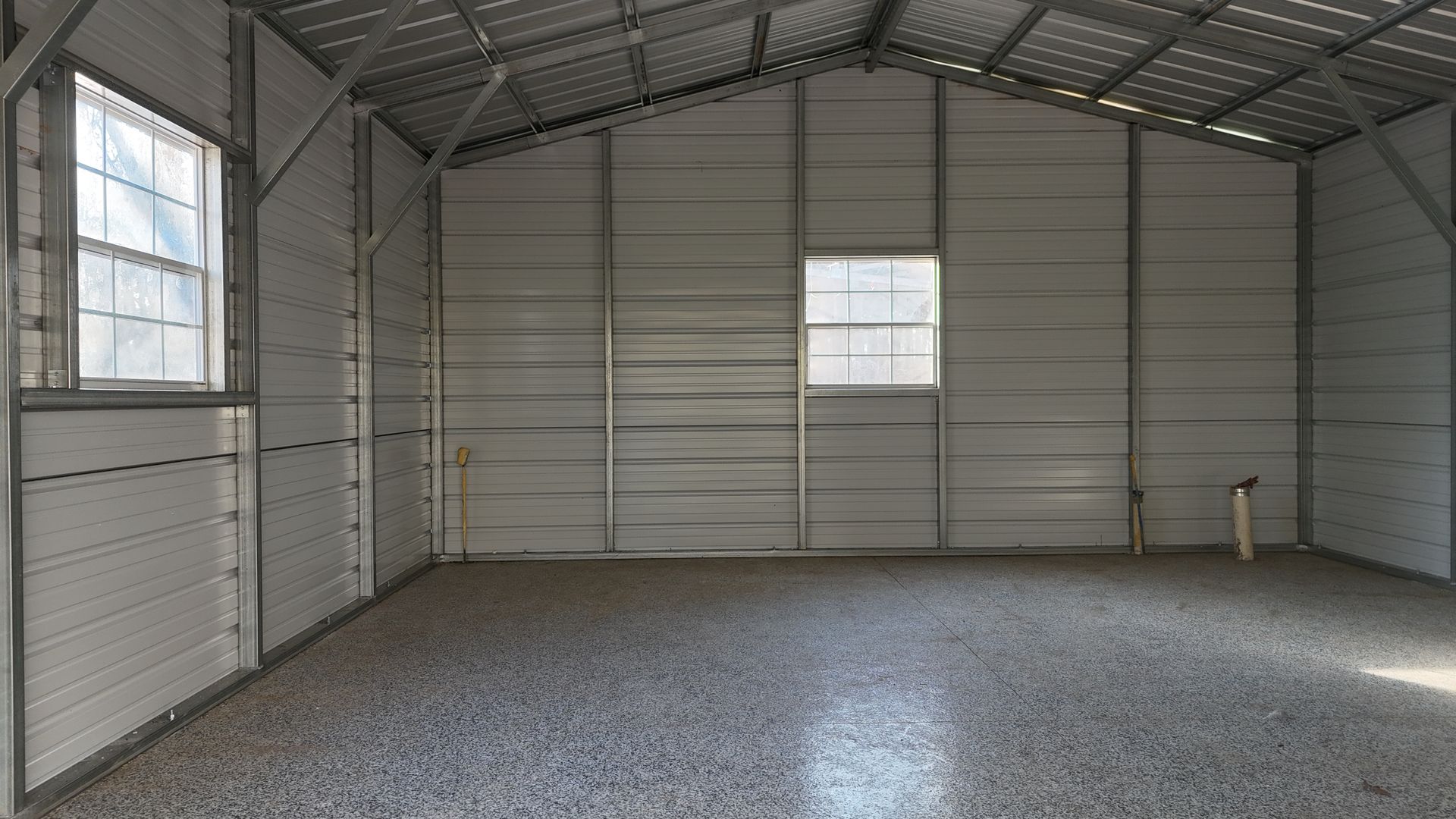Inside a metal shed, gray gravel floor, windows, and corrugated metal walls.