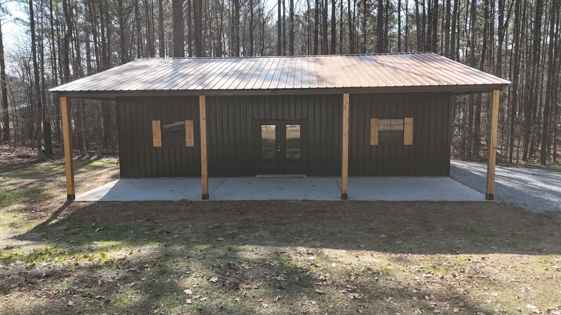 Dark cabin with a porch under a metal roof, set in a forest.