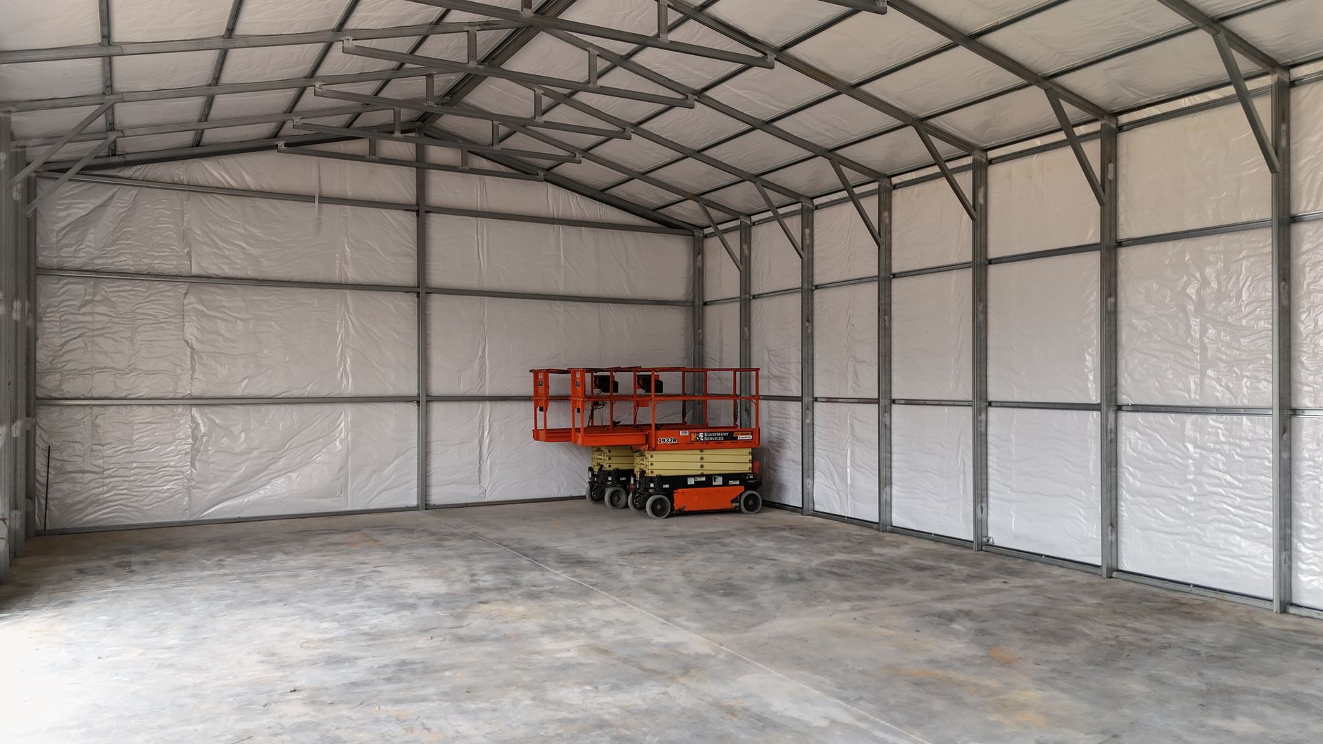 Interior of a large metal building with gray concrete floor, white insulated walls, and a lift.