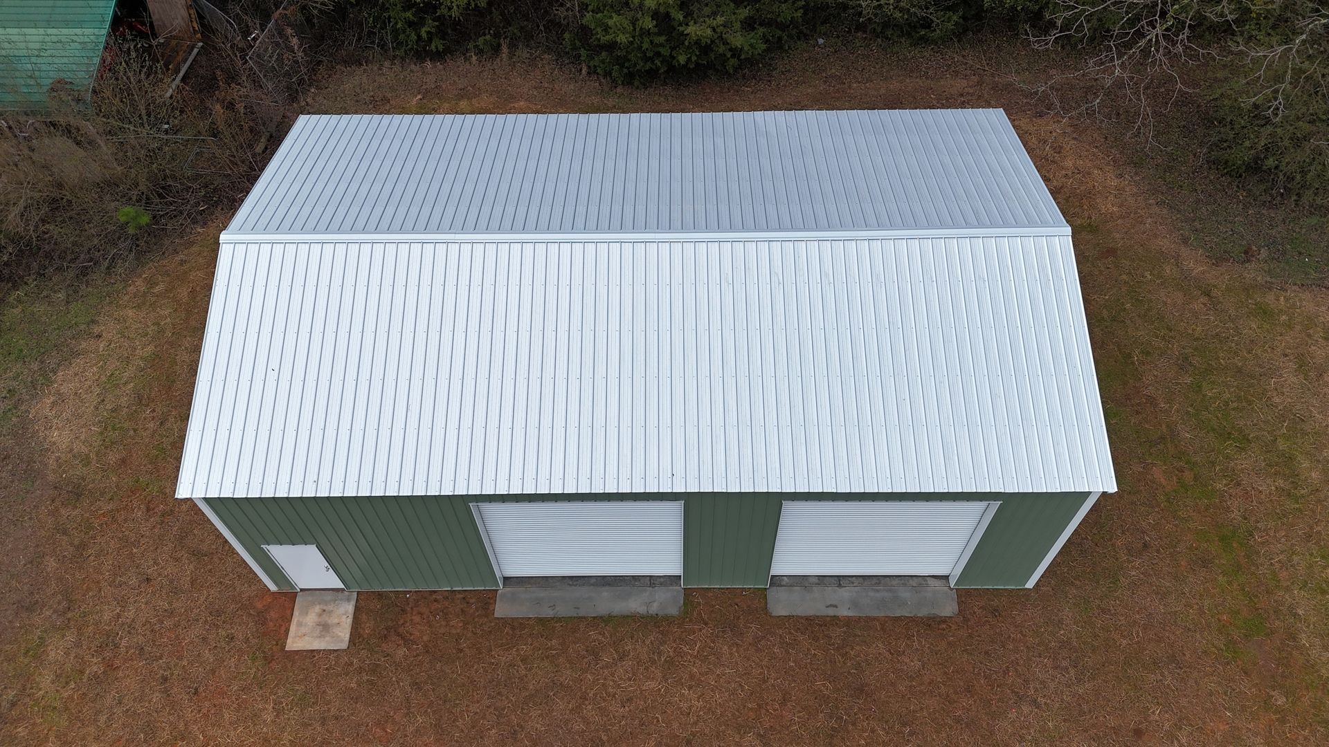Green metal building with two garage doors and a corrugated metal roof.