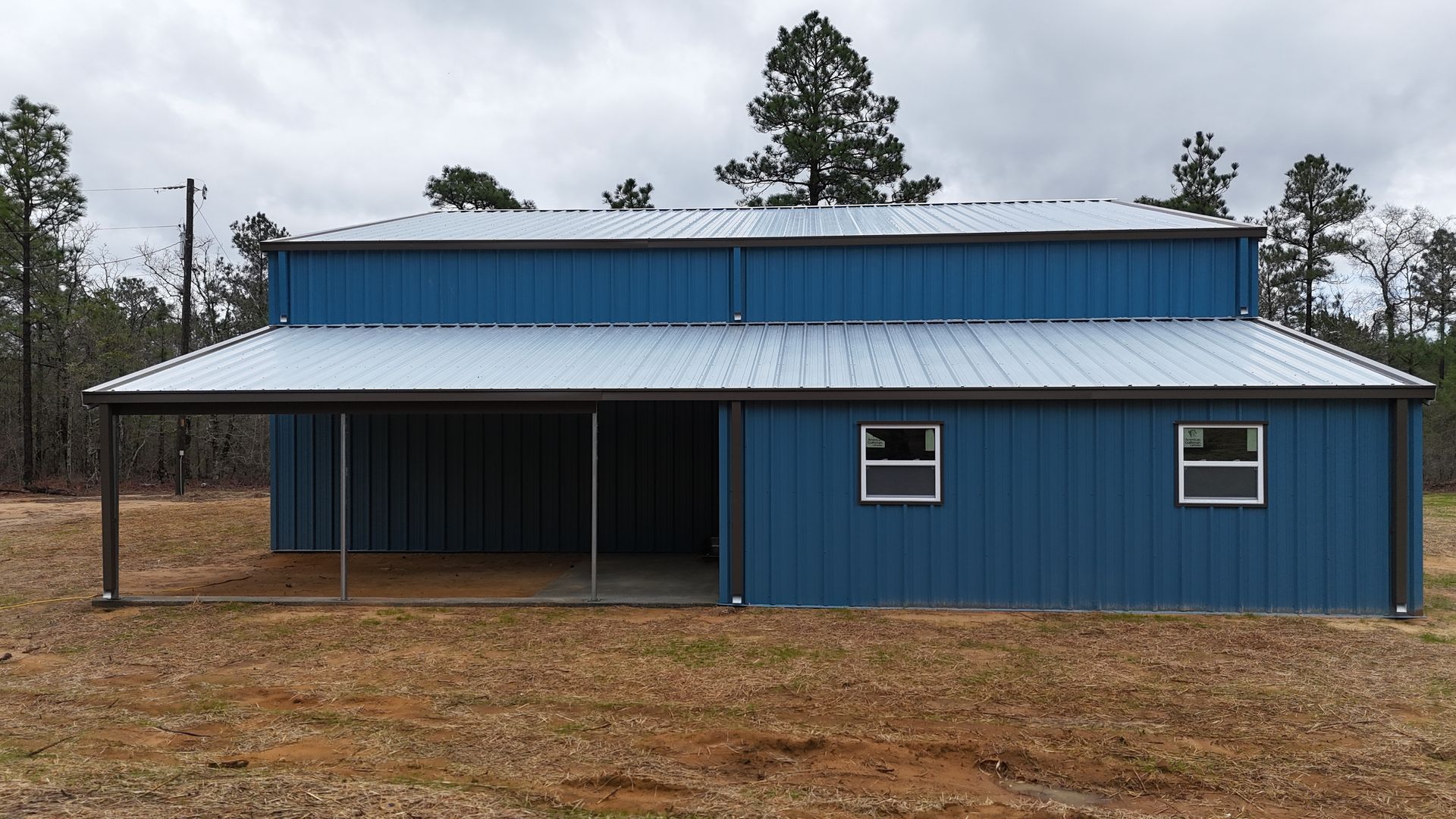 Blue metal barn with a covered porch under a cloudy sky.