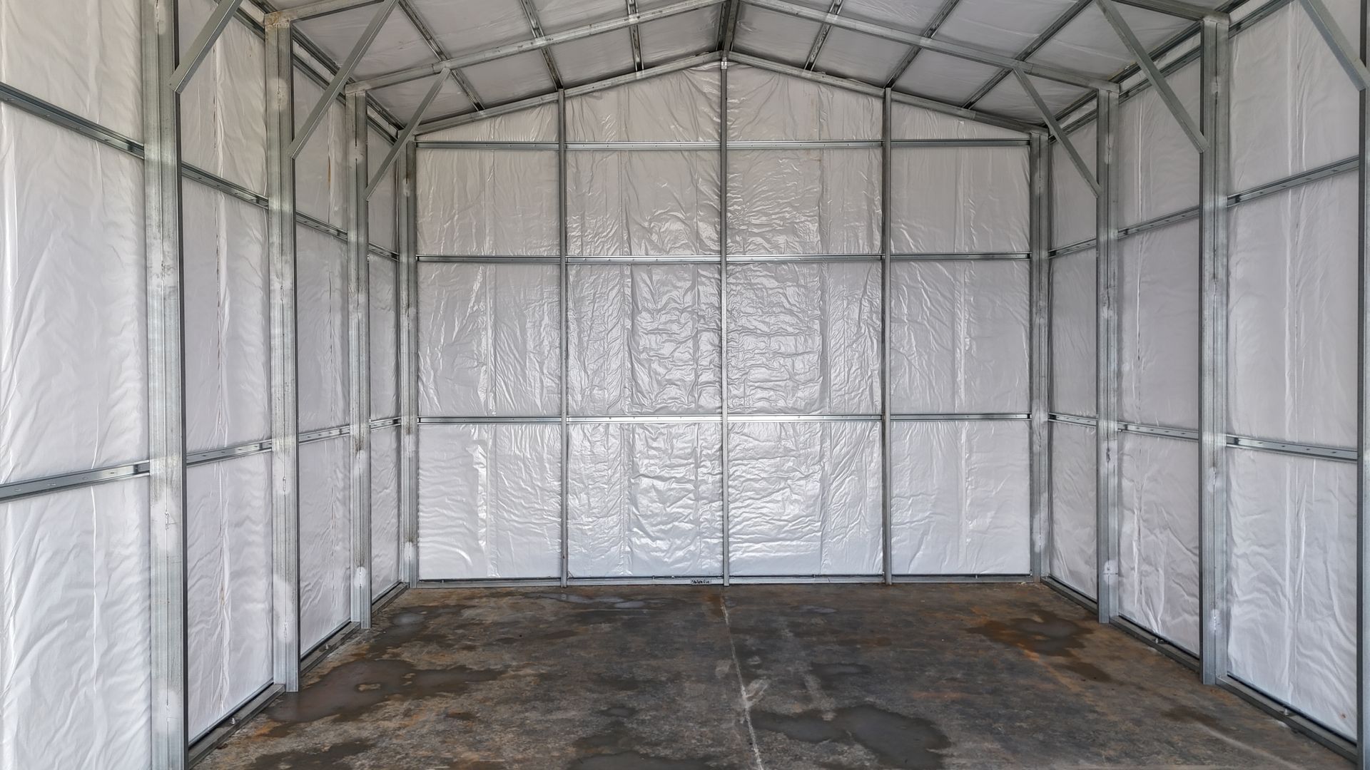 Interior of a metal building with a steel frame, white wall insulation, and a concrete floor.