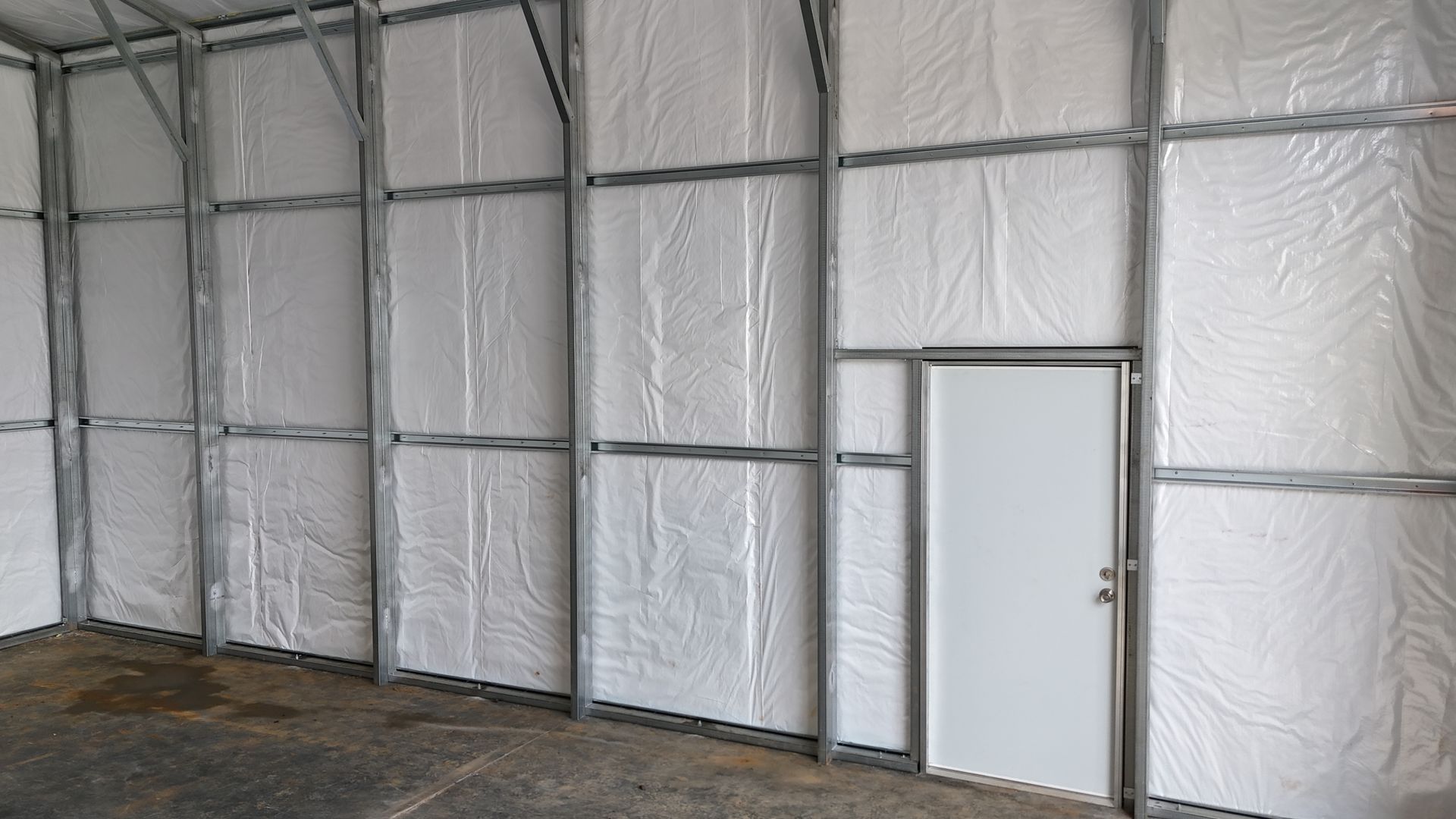 Interior view of a building with metal frame walls covered in white insulation, featuring a single white access door.