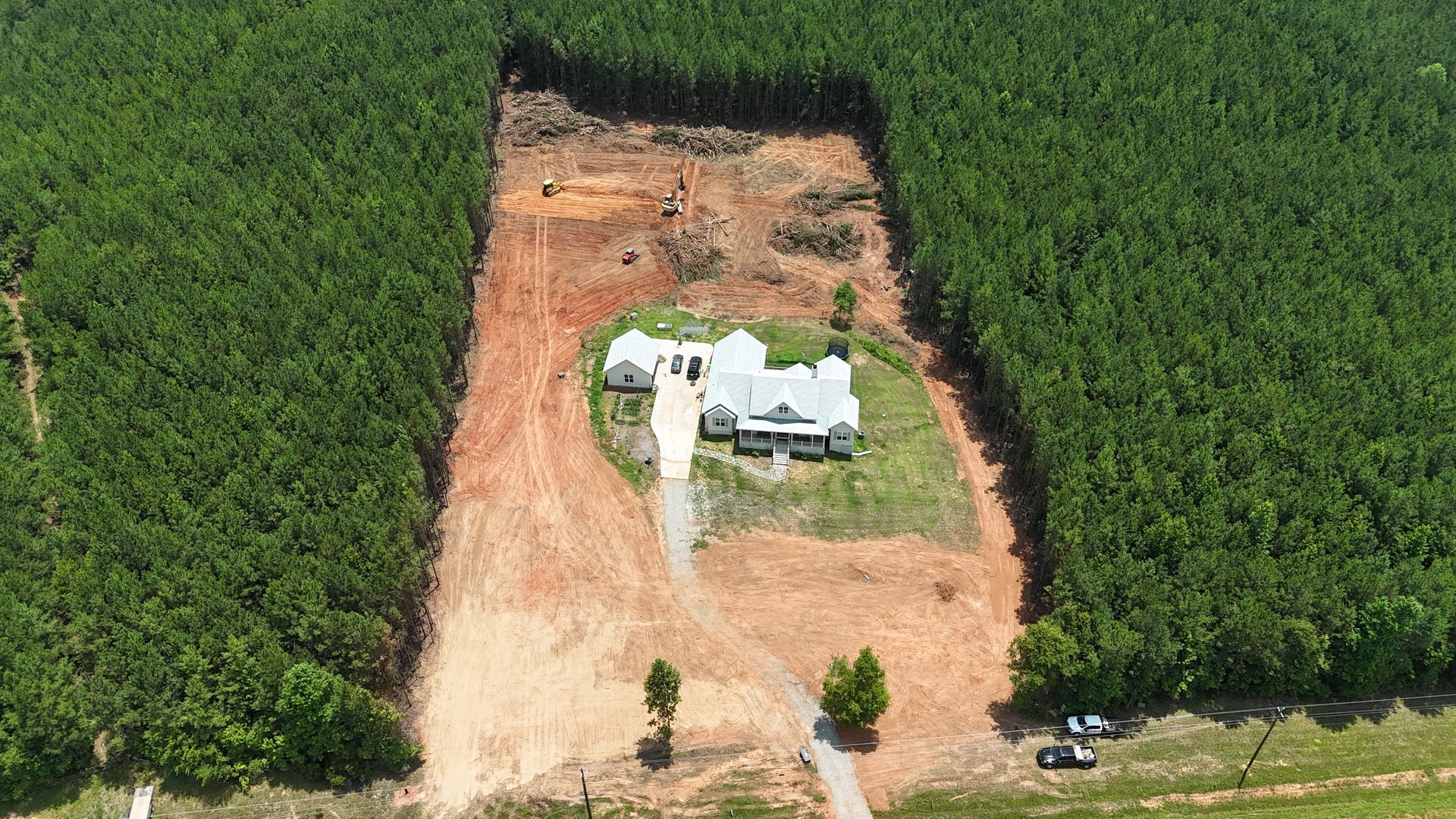 A white house sits in a cleared patch amid dense green farmland, viewed from above.