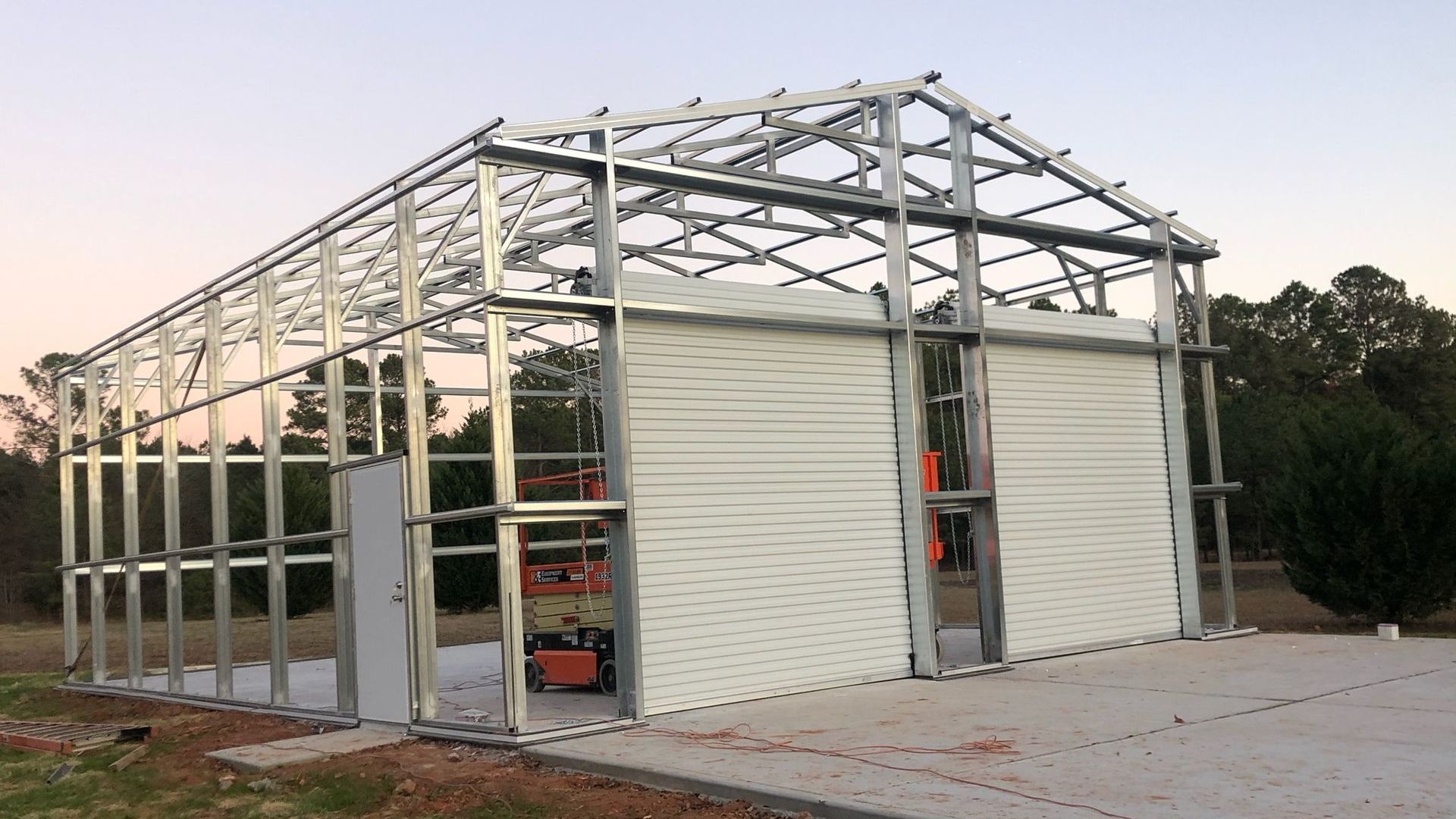 A large metal building is being built on a dirt road.