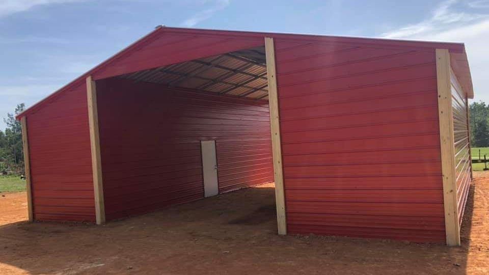 A large red barn is sitting in the middle of a dirt field.