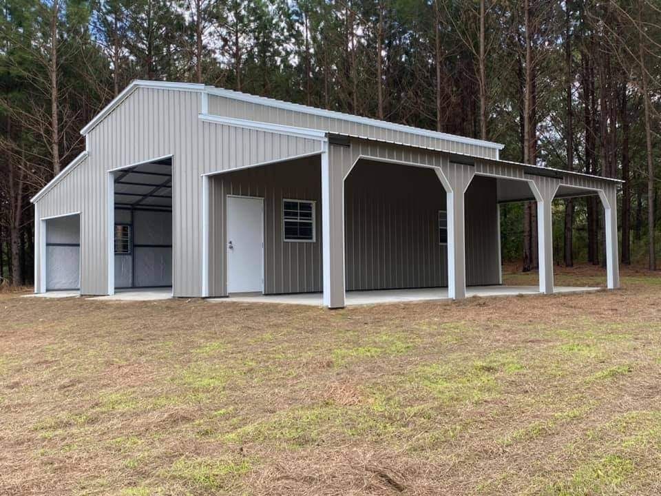 A large metal building with a porch is sitting in the middle of a grassy field.