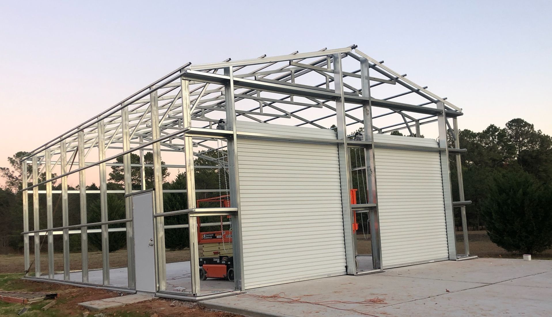 A large metal building frame with a sliding garage door is being built.