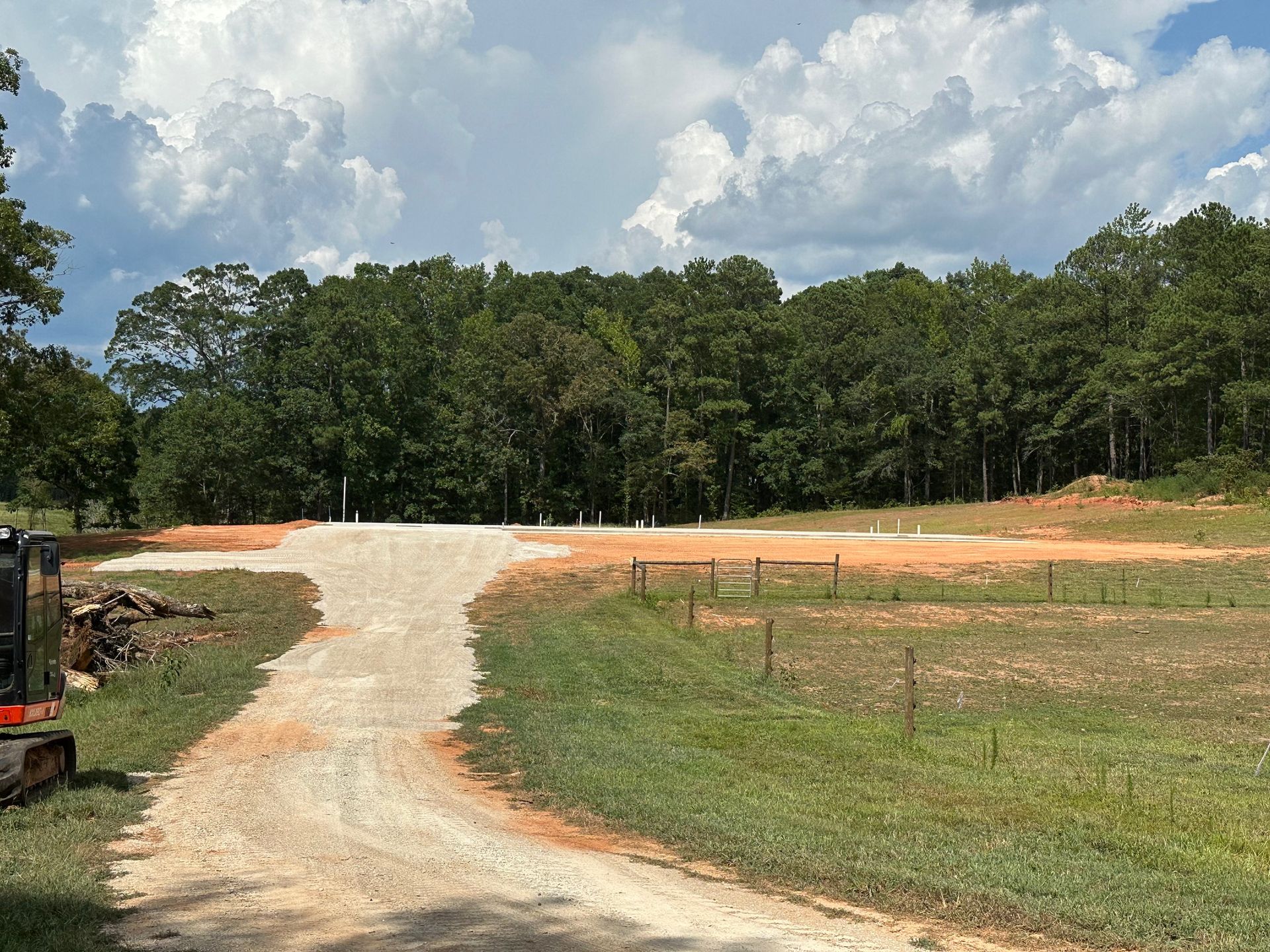 A dirt road going through a grassy field with trees in the background.