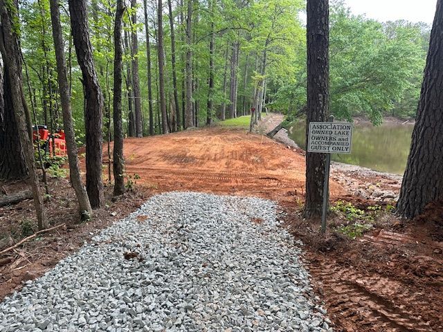 A gravel road in the middle of a forest next to a lake.
