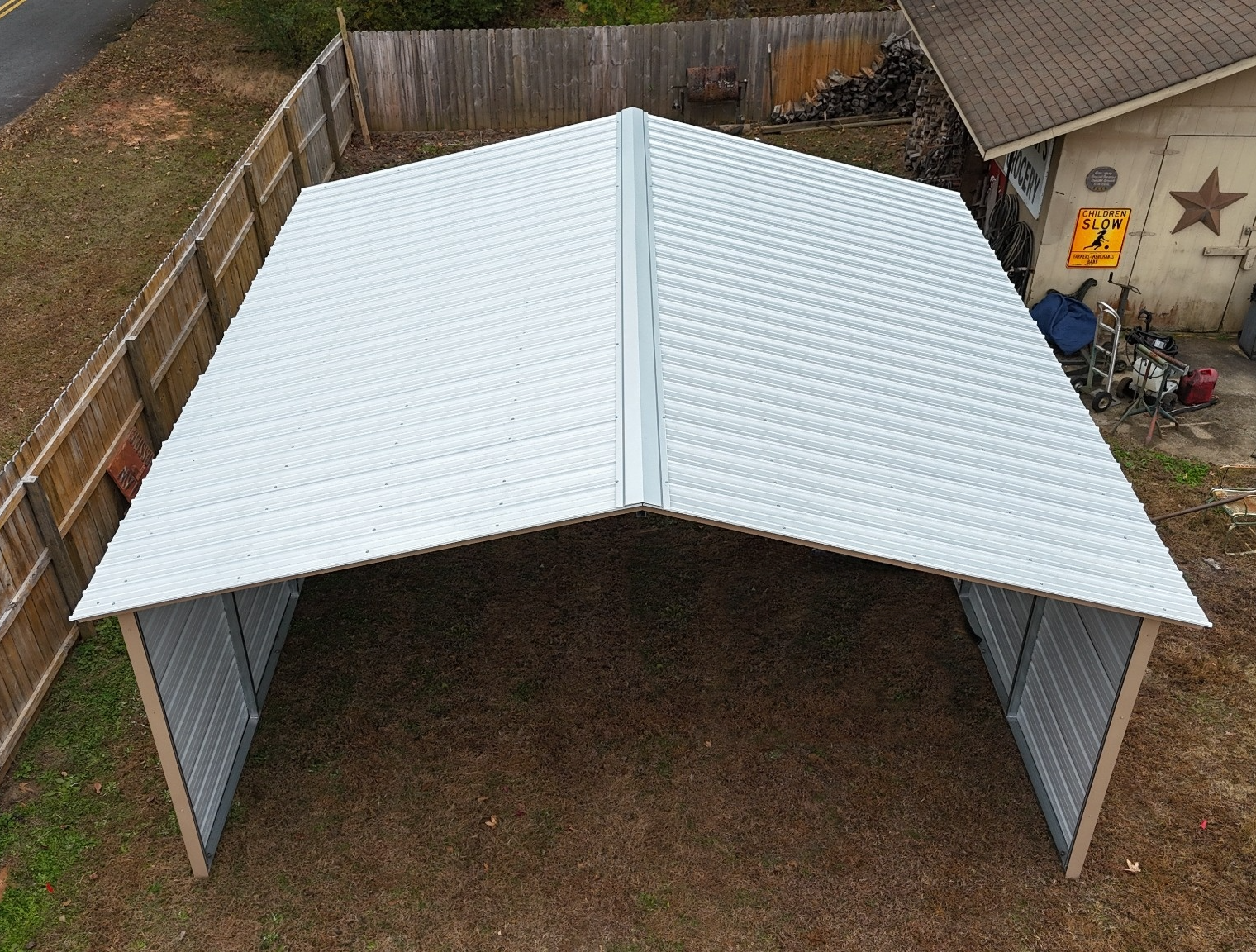 A metal carport in a backyard, with a sloped roof and open sides.