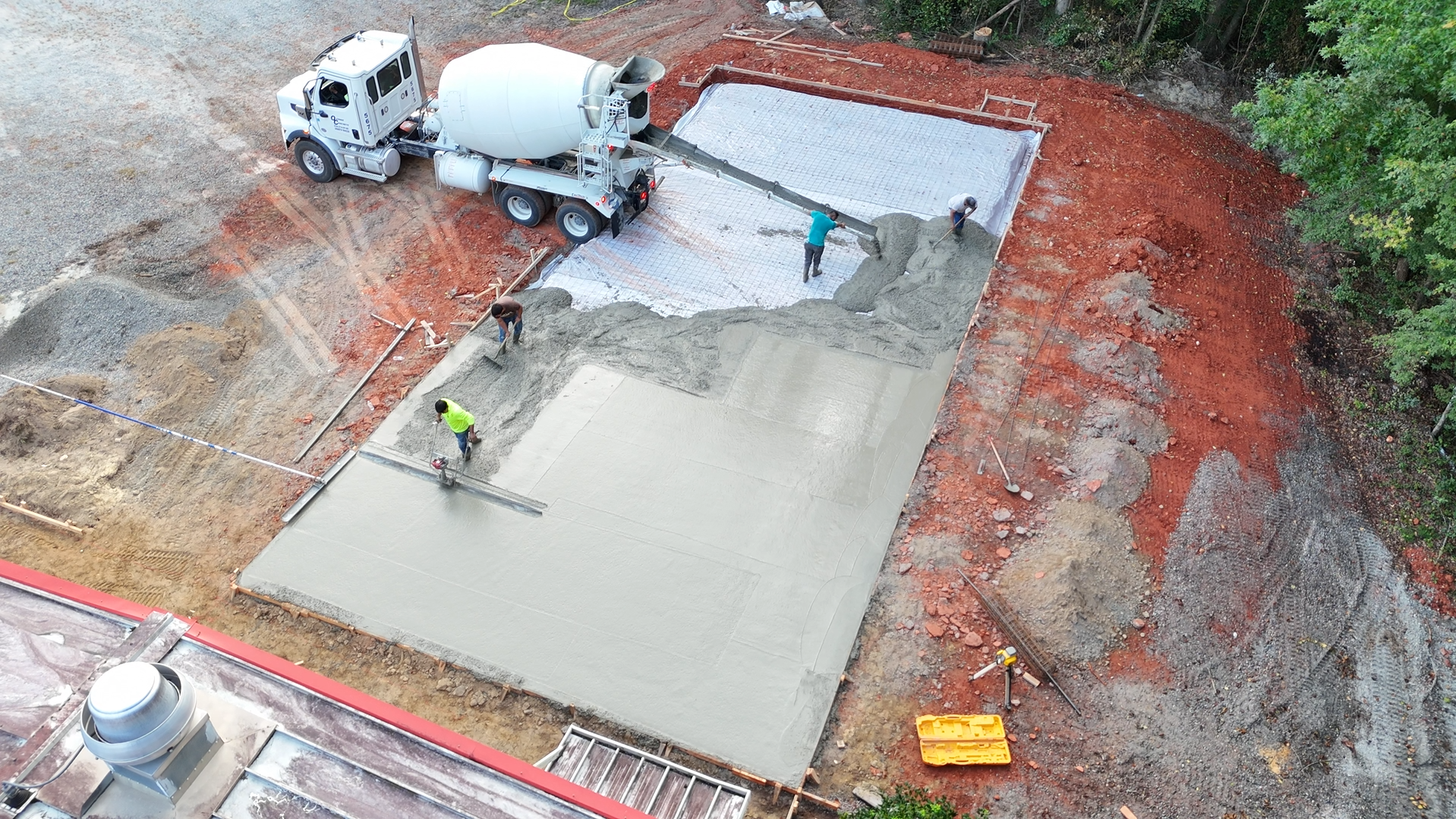 Concrete being poured from a truck onto a prepared site by construction workers.