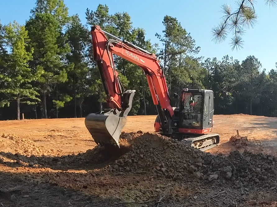 A red and black excavator is digging in a dirt field