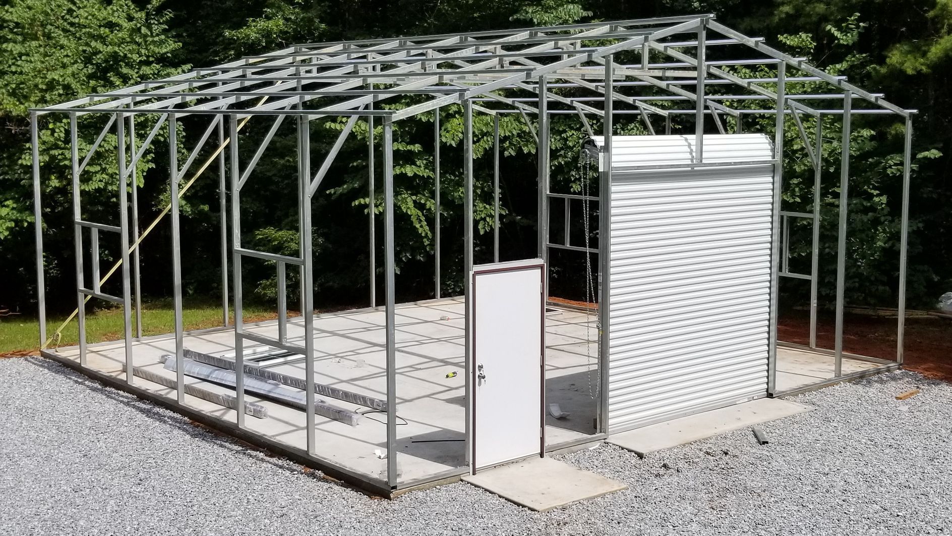 A metal garage is being built in a gravel lot.