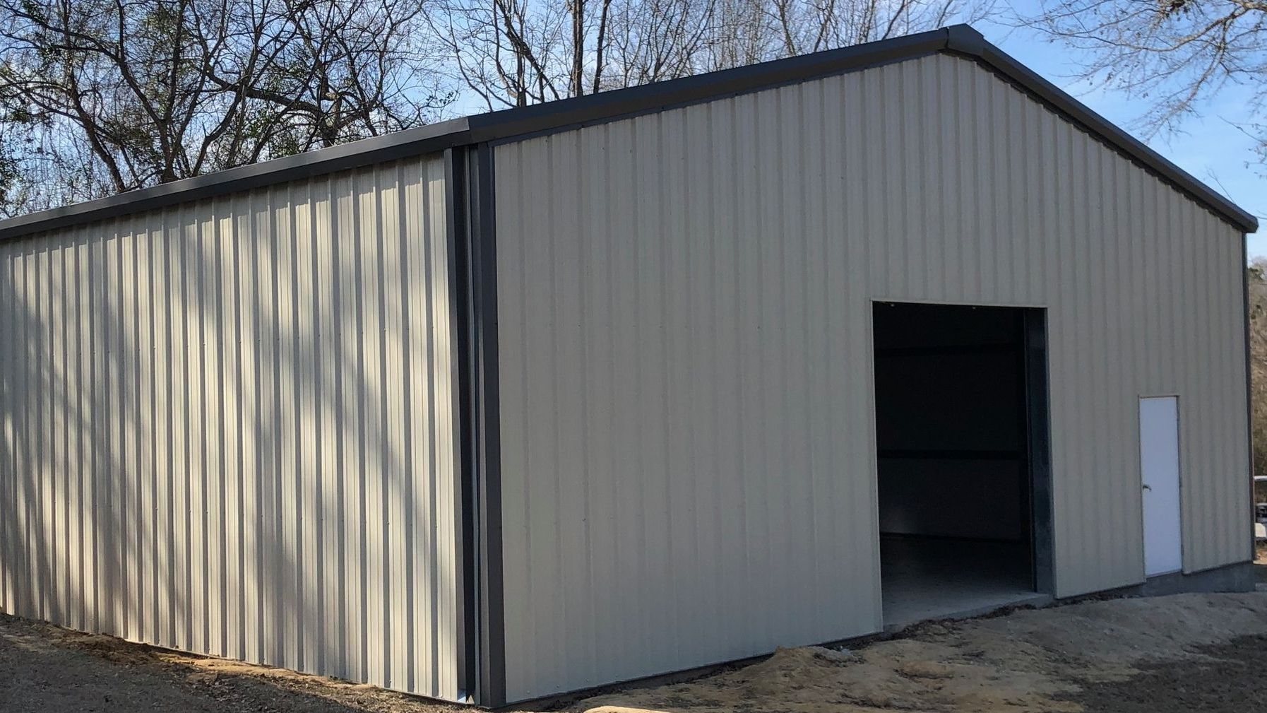 A large metal building with a large door and trees in the background.