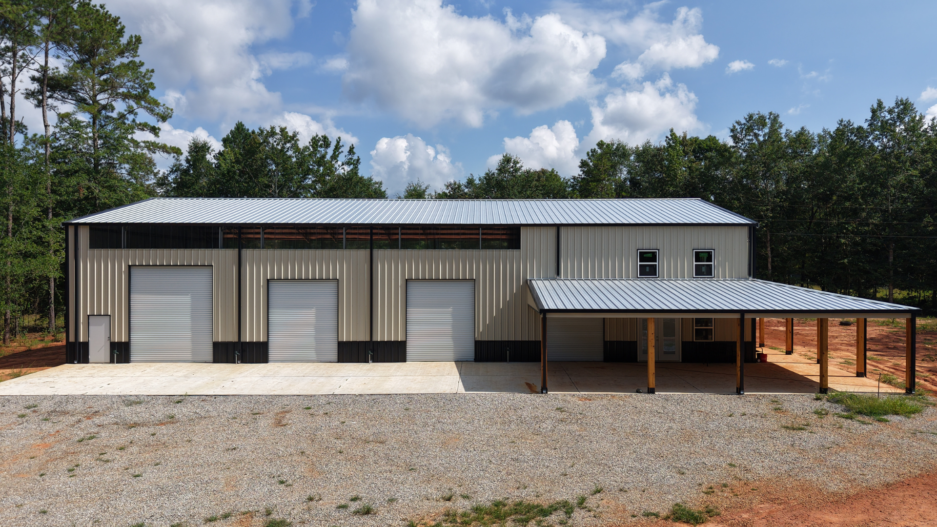 Metal building with three garage doors and a covered porch under a blue sky.