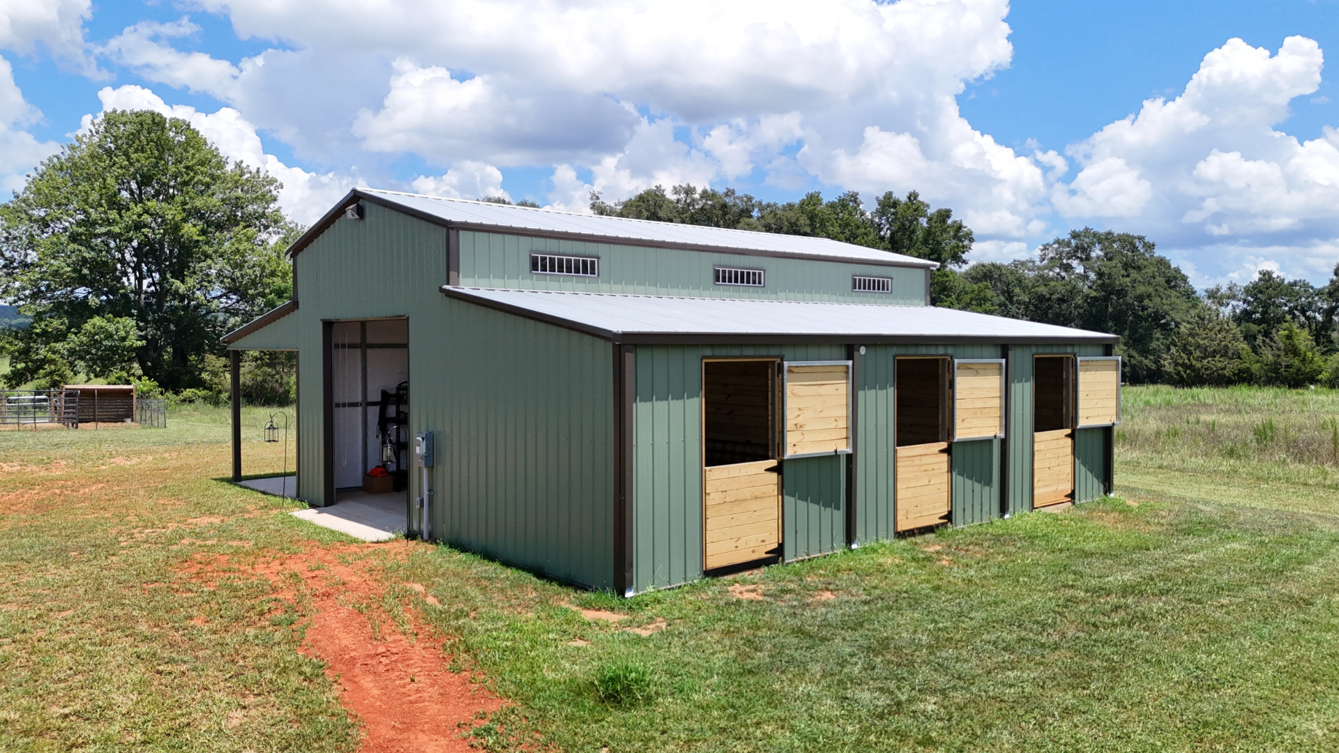 Green metal barn with horse stalls, silver roof, and tan wooden shutters.