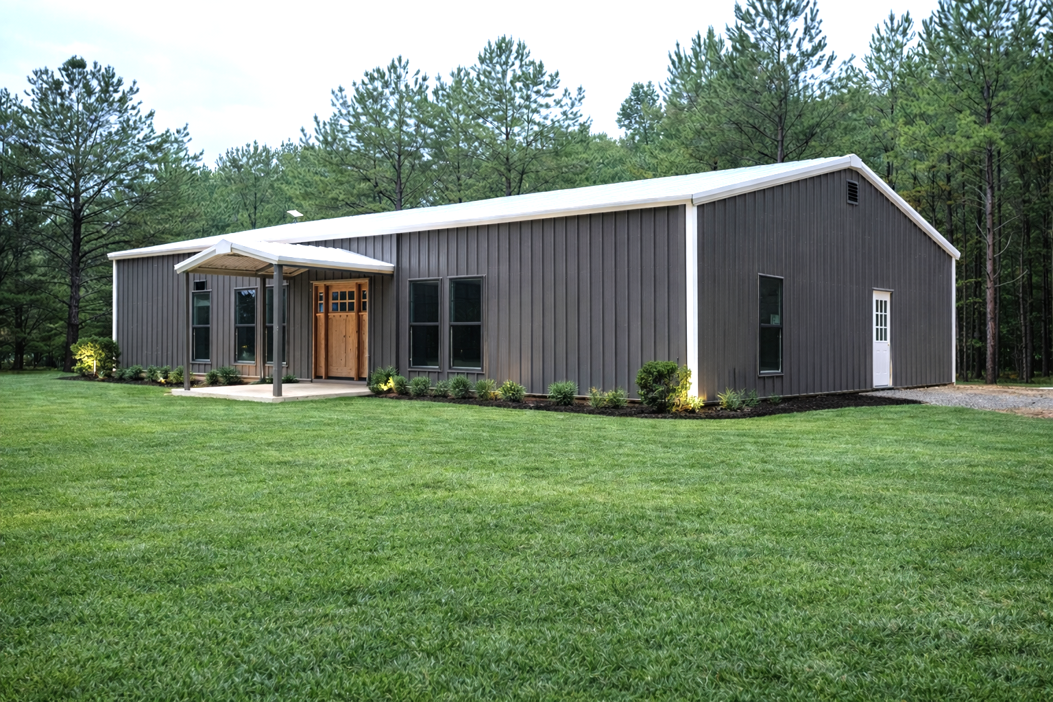 Gray metal building with white trim, door, windows, and manicured lawn.