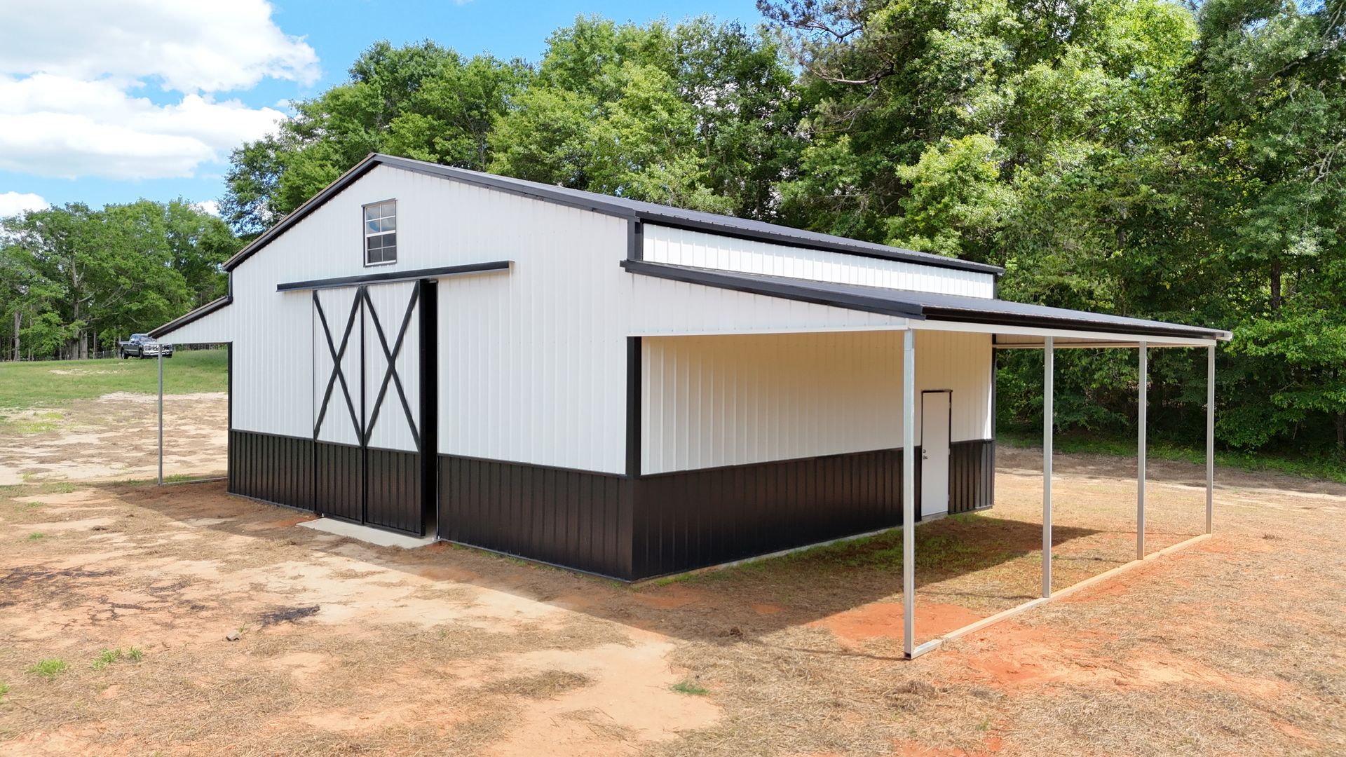 A white and black barn with a covered porch in a field.