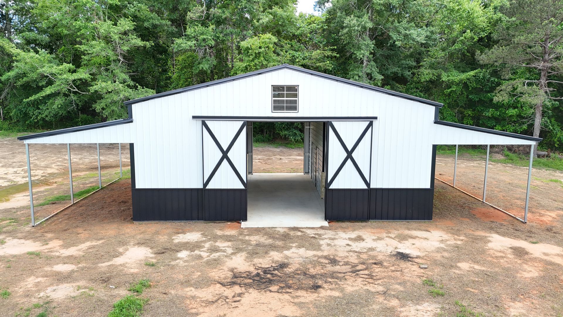 A white and black barn is sitting in the middle of a dirt field.