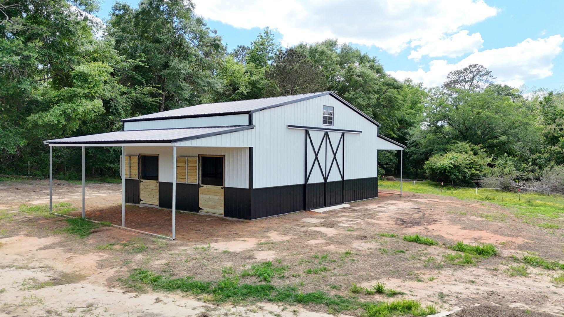 A white and black barn with a covered porch in a field.
