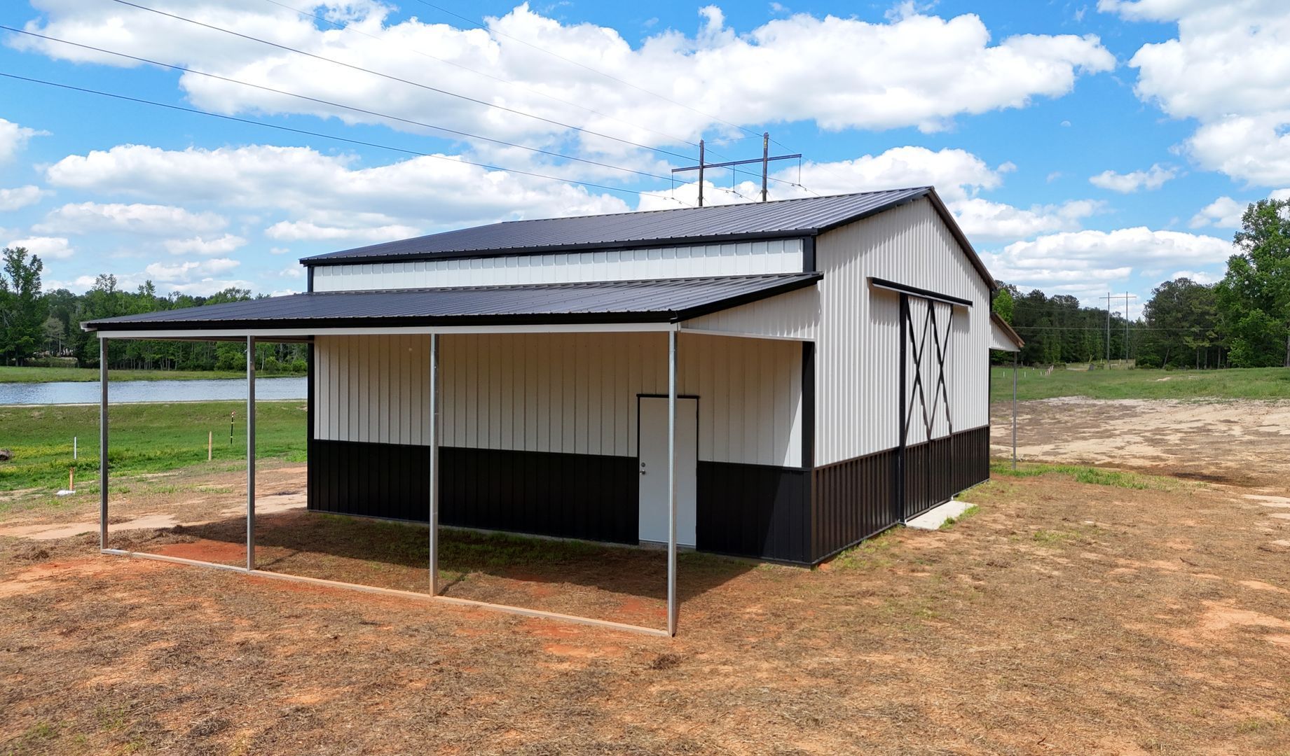 A white and black barn with a porch is sitting in the middle of a field.