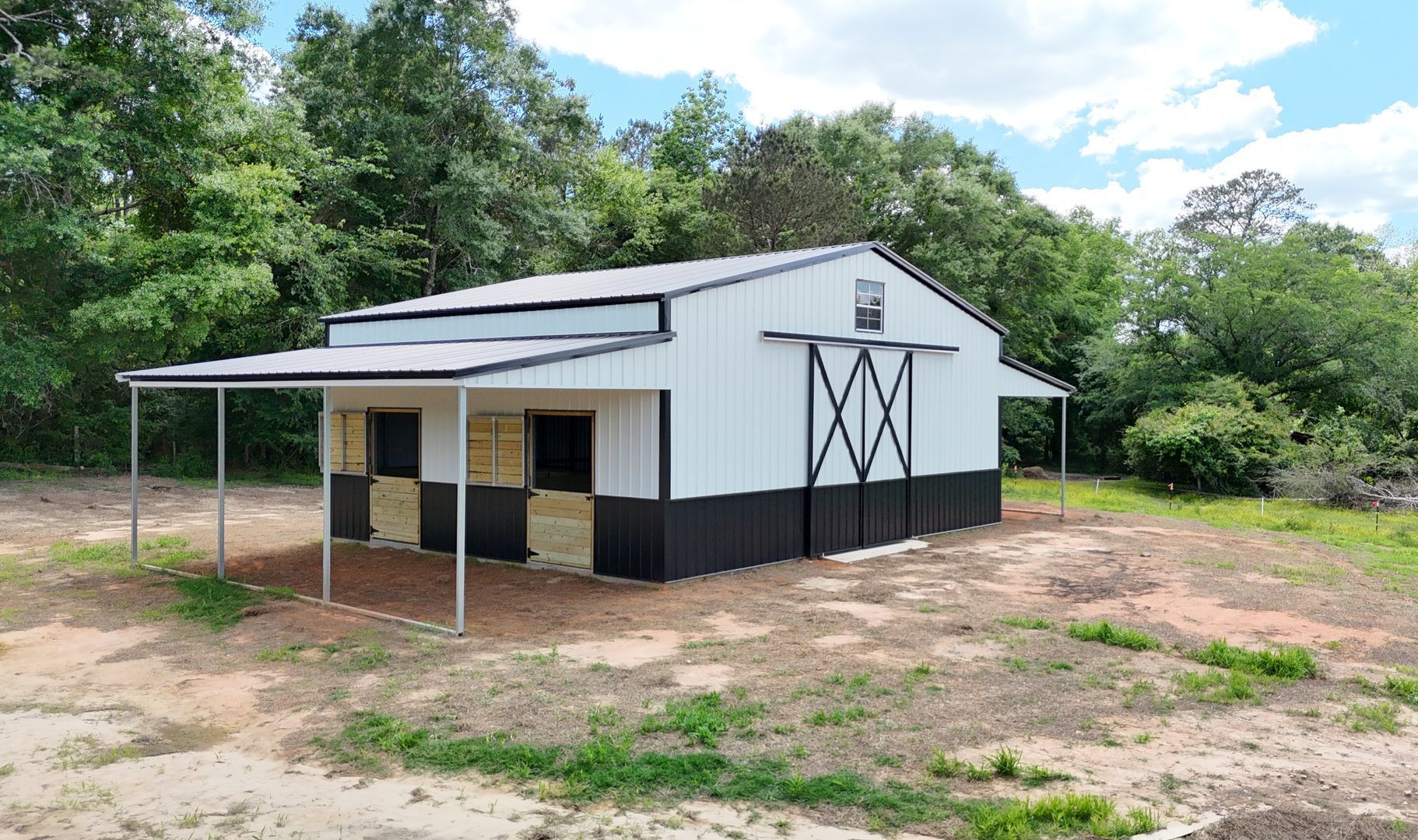 A white and black barn with a porch in a field.