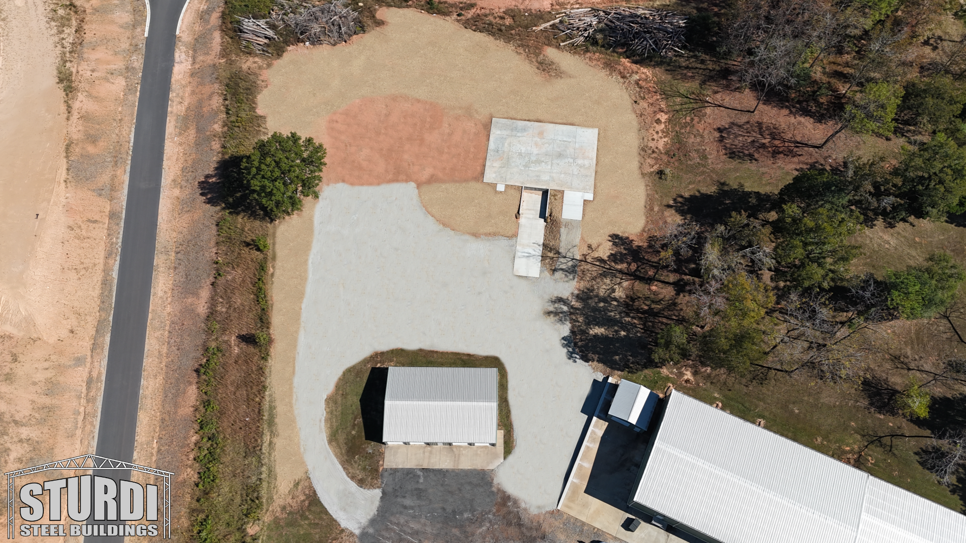 Overhead view of a dirt area with gravel parking, a small building, and a canopy.