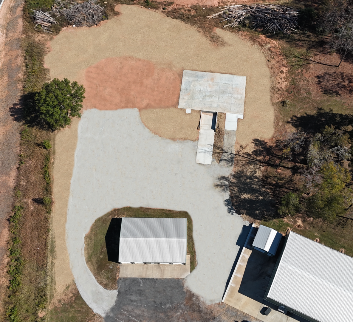 Overhead view of a dirt area with gravel driveway and buildings, some with white metal roofs.
