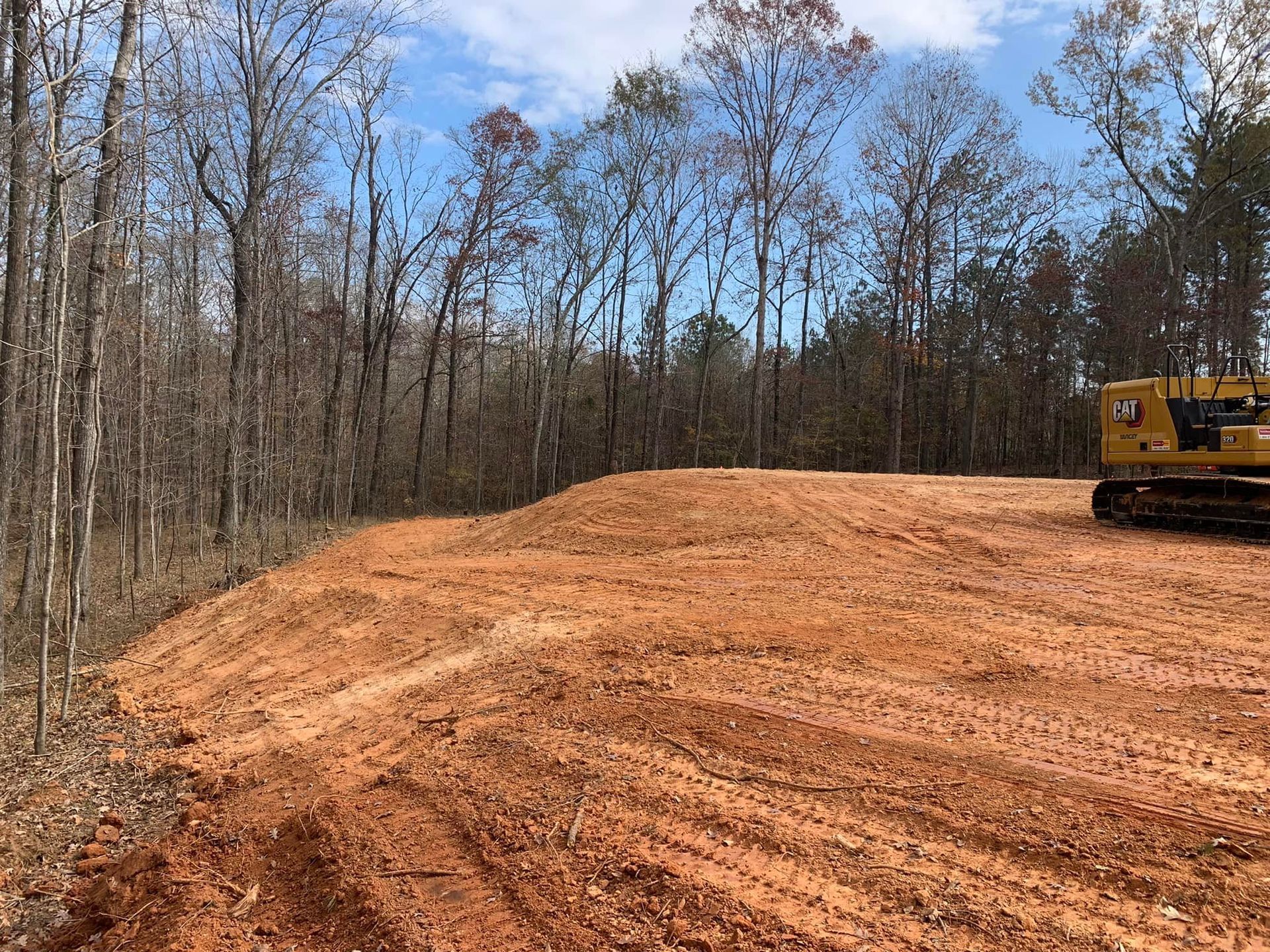 A bulldozer is sitting on top of a dirt hill in the middle of a forest.