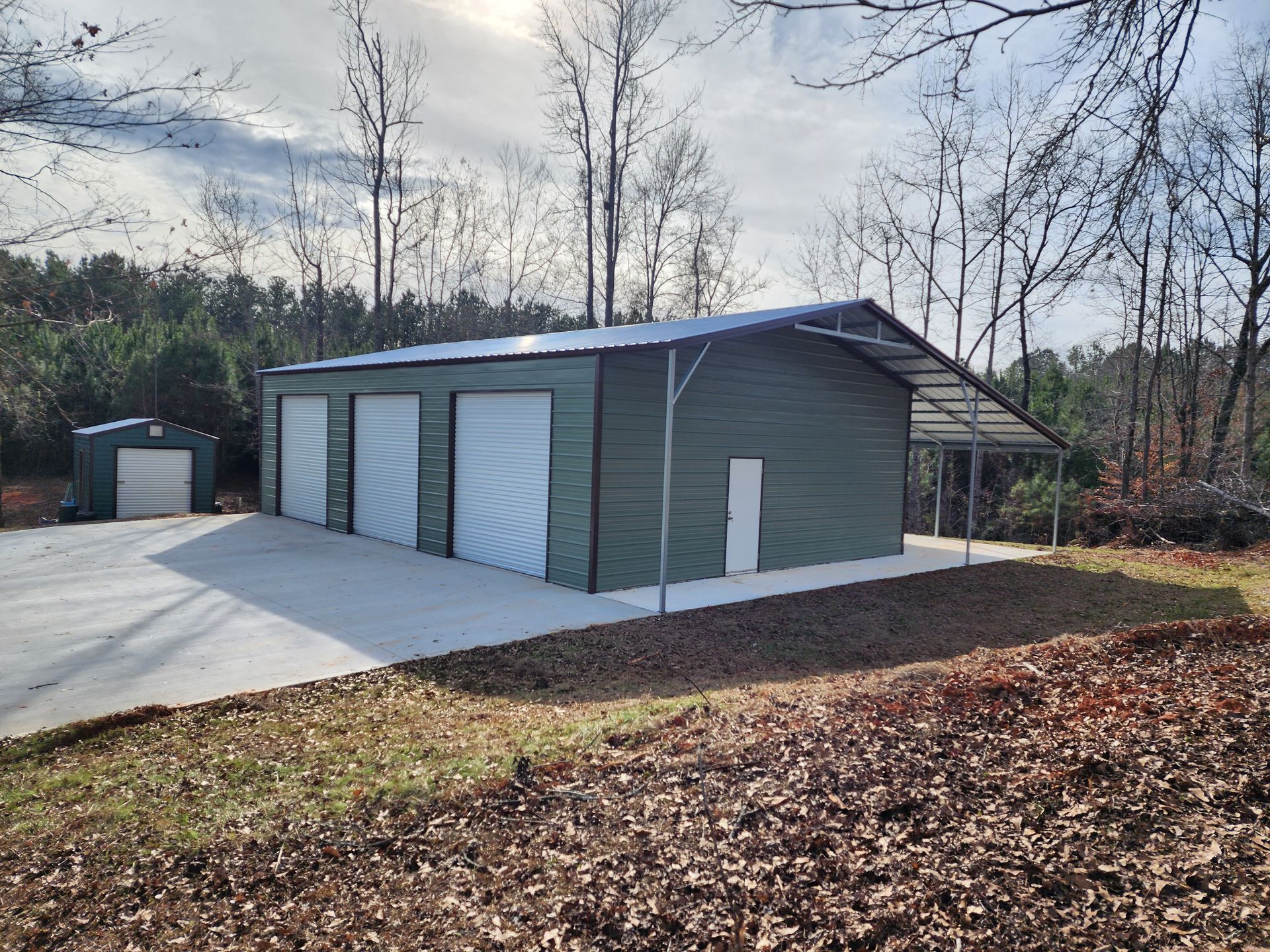 A green garage with white doors is surrounded by trees and leaves.