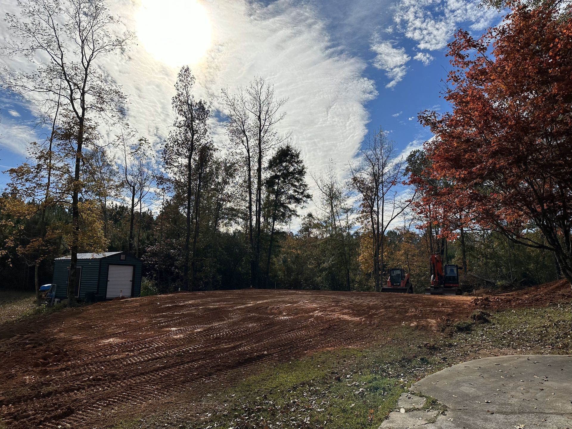 A dirt field with trees in the background and the sun shining through the clouds.