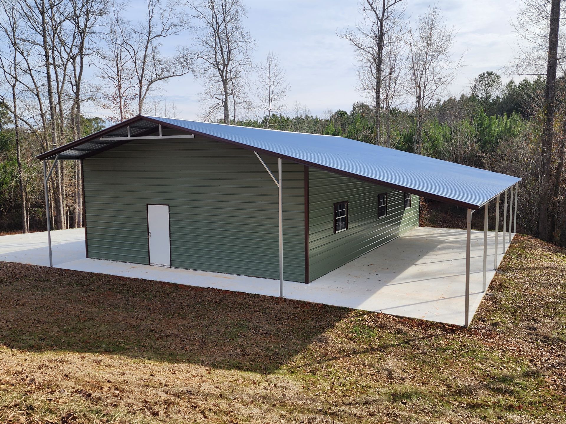 A metal building with a blue roof is sitting in the middle of a field.