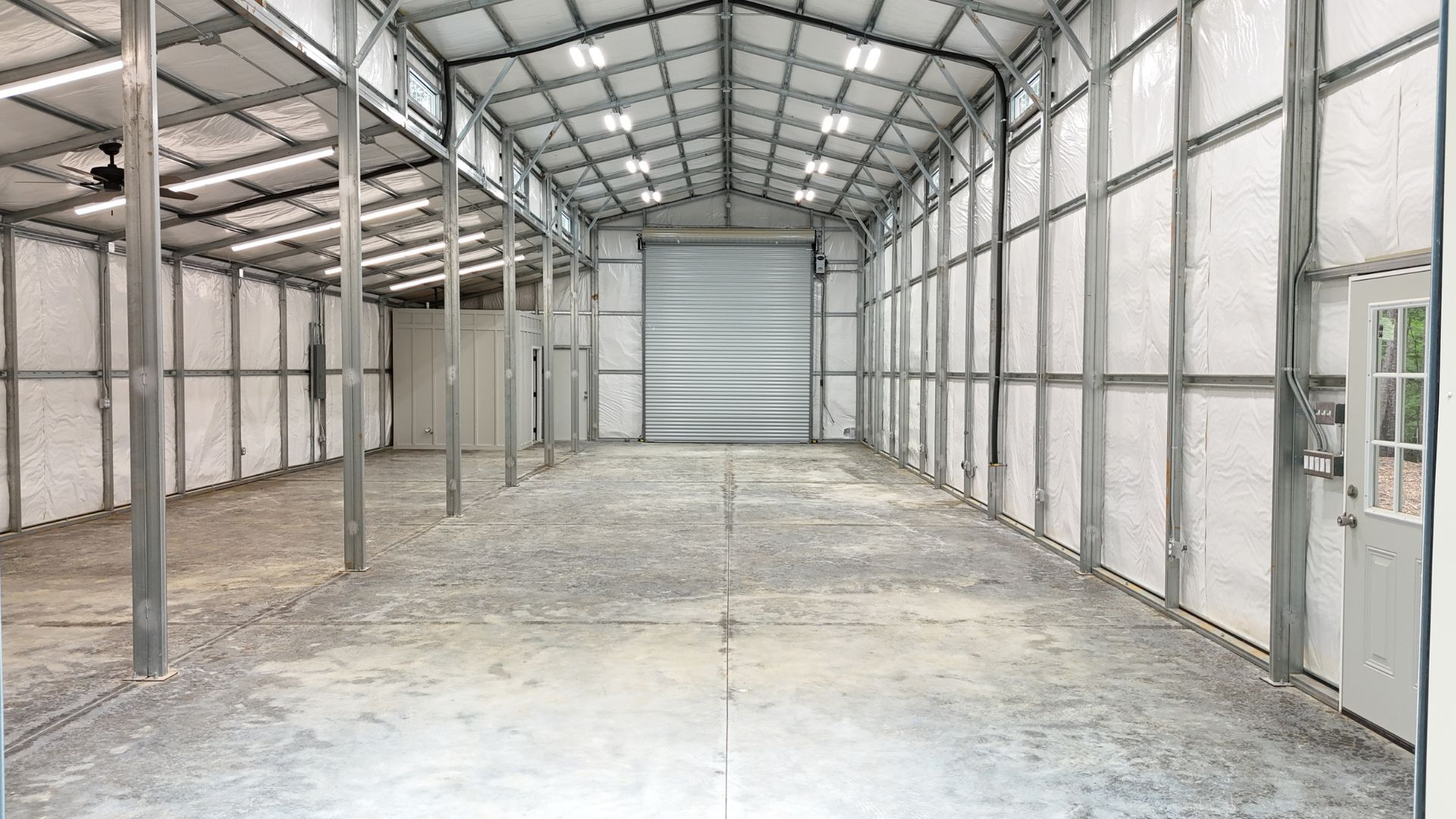 An empty warehouse with a garage door and a ceiling fan.