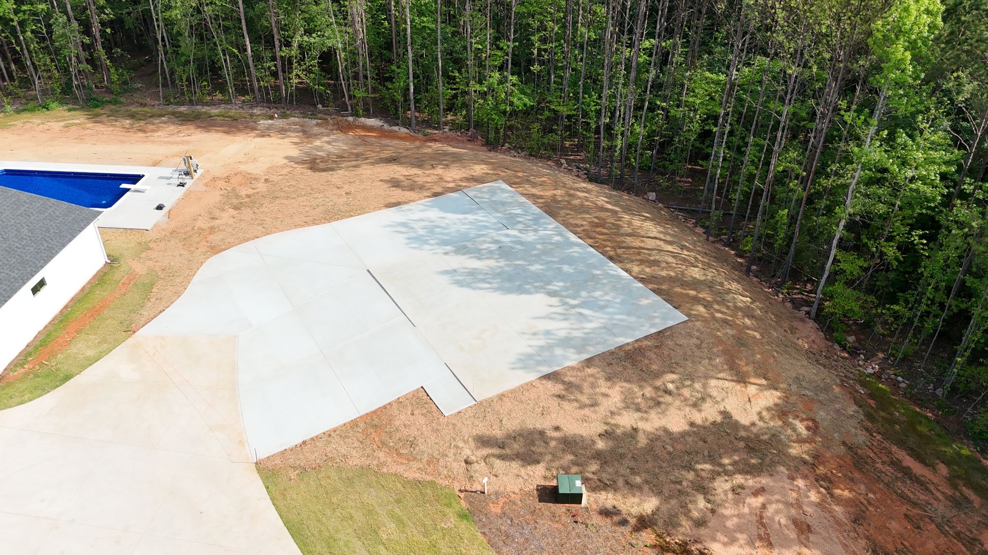 An aerial view of a driveway leading to a swimming pool surrounded by trees.