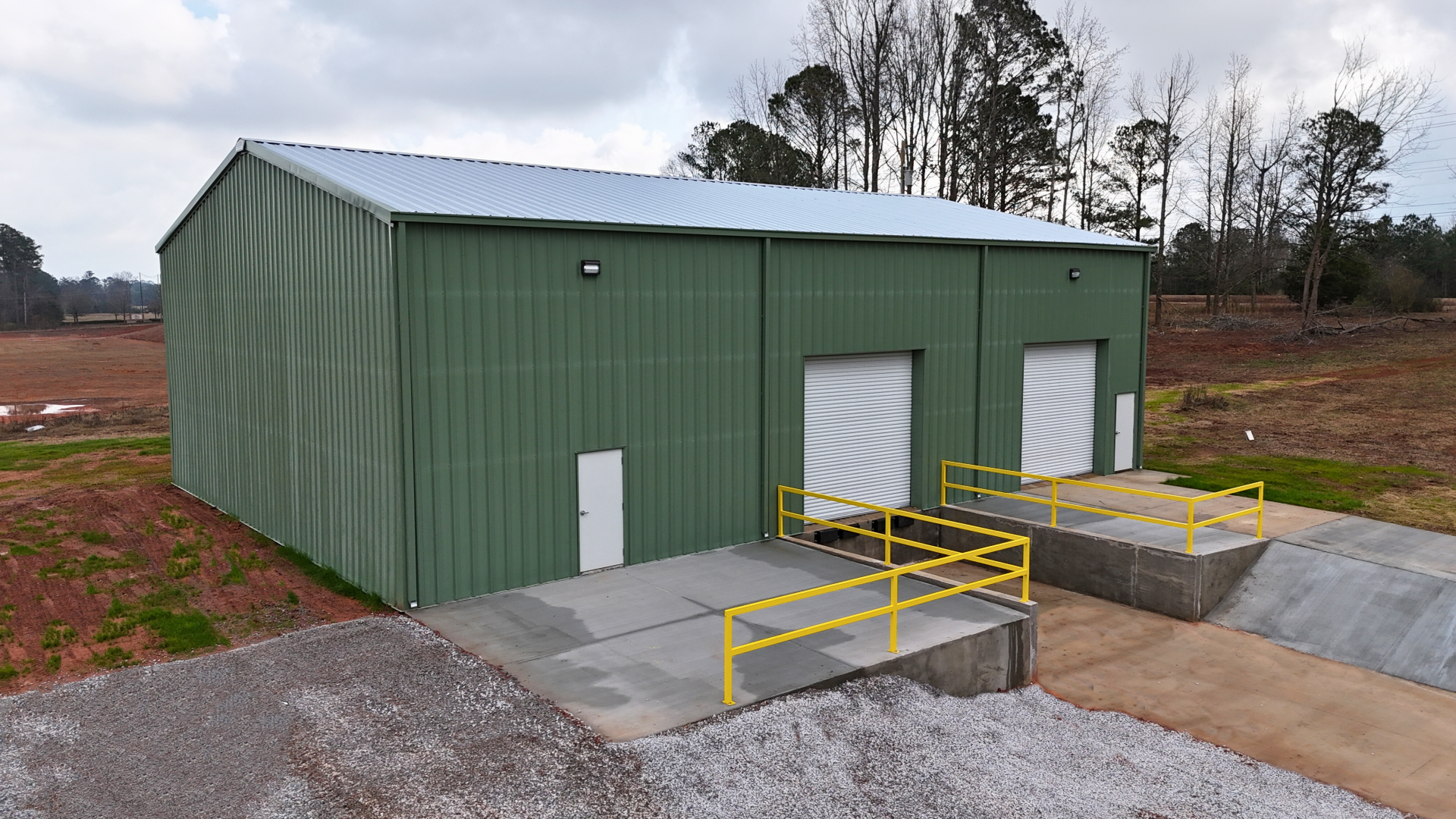 Green metal warehouse with loading docks, two overhead doors, and a metal roof.