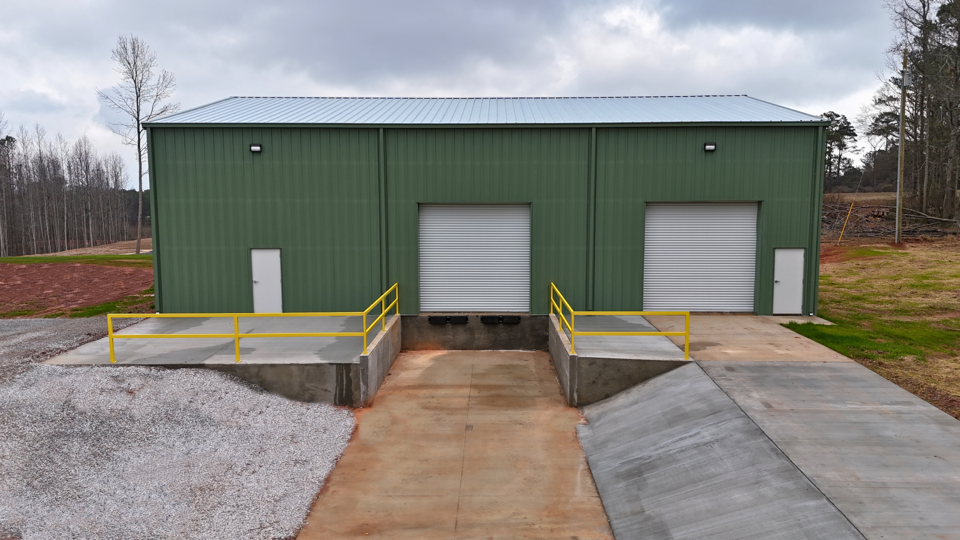 Green metal building with two loading docks and roll-up doors, concrete ramps, and a gravel base.
