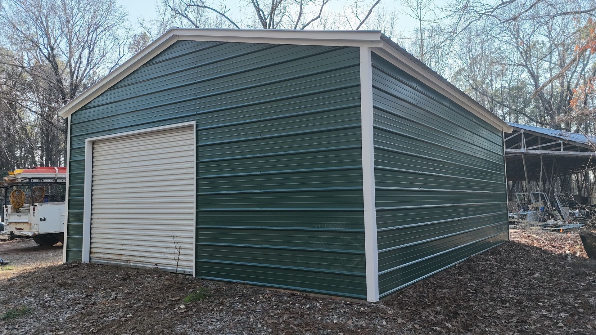 Green metal garage with a white roll-up door. White trim accents the roofline and corners; brown yard.